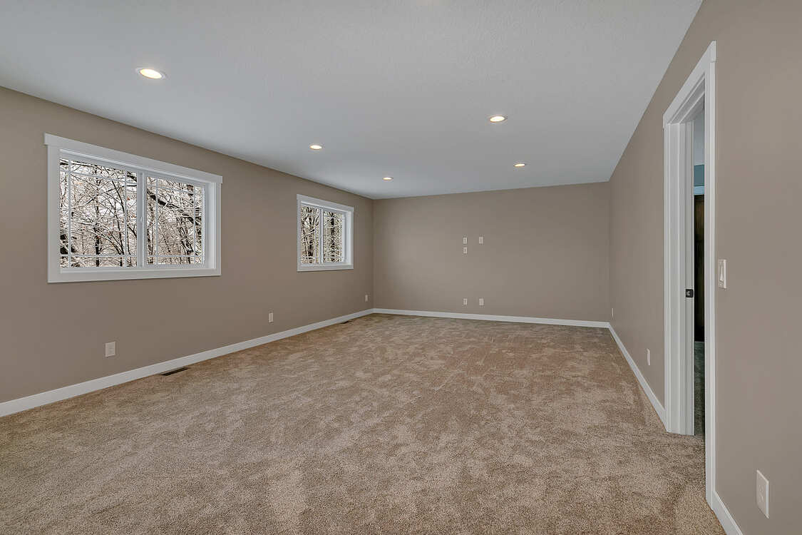 An empty room with a carpeted floor and two windows.