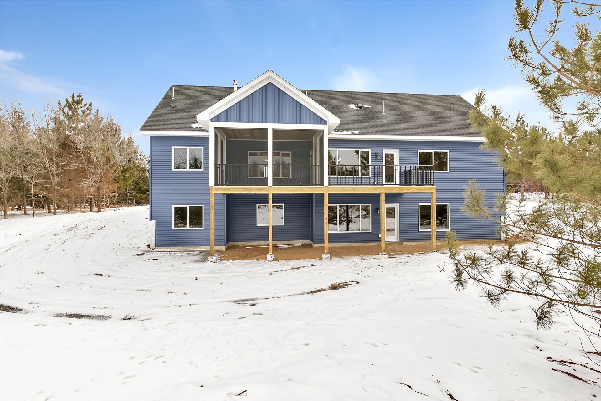 A large blue house with a large deck in the snow.
