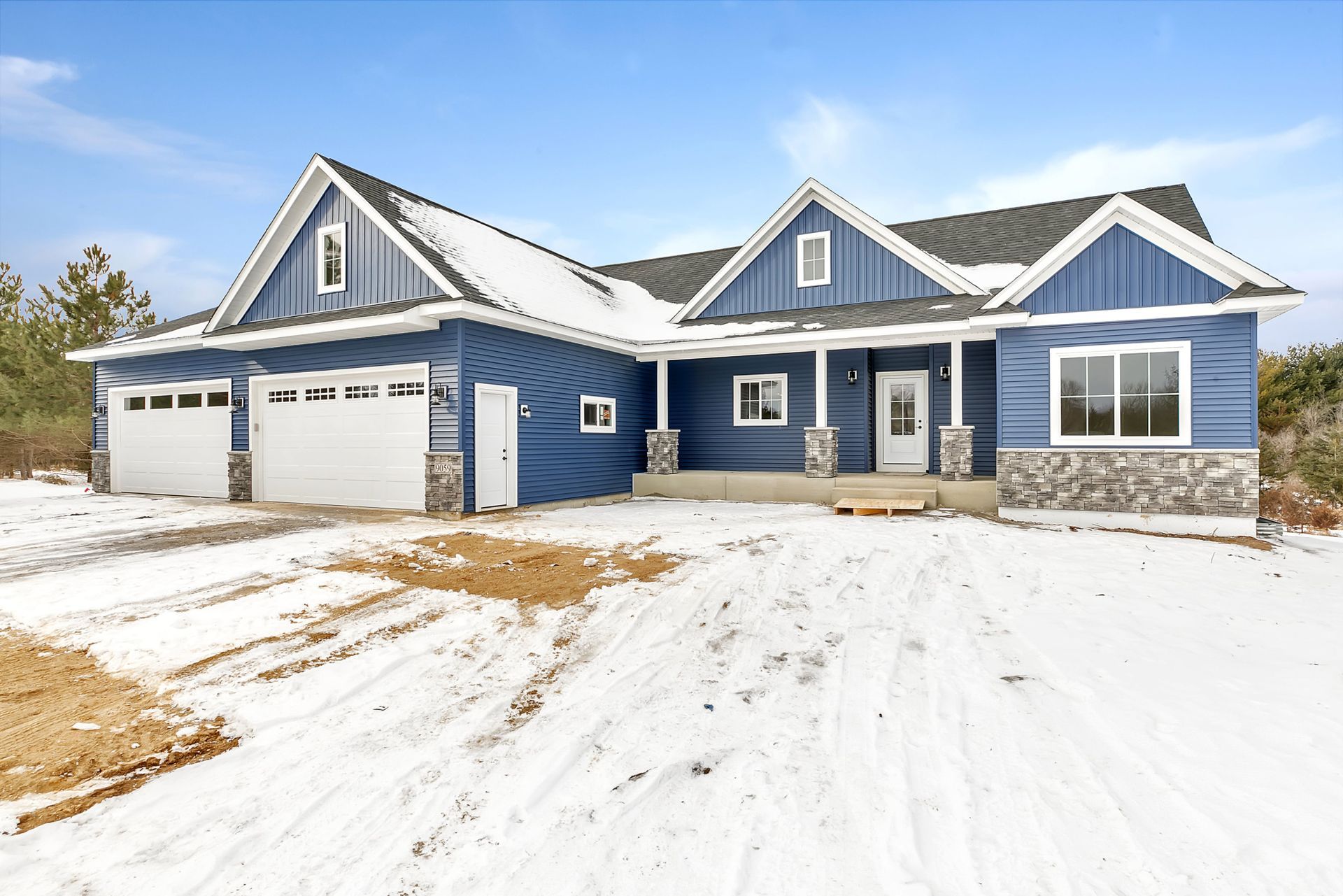 A blue house with two garages is sitting in the snow.