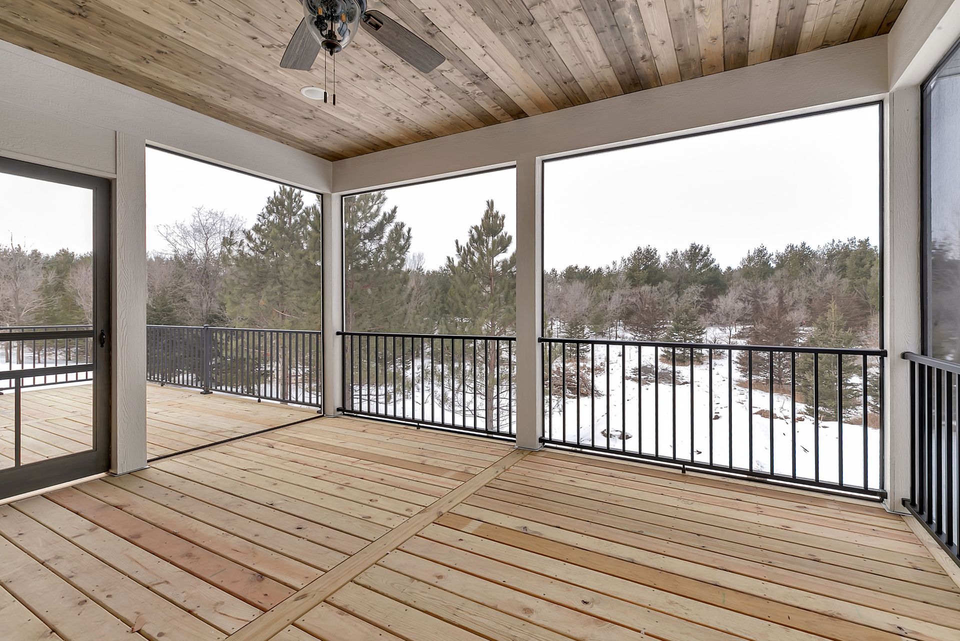 A screened in porch with wooden floors and a ceiling fan