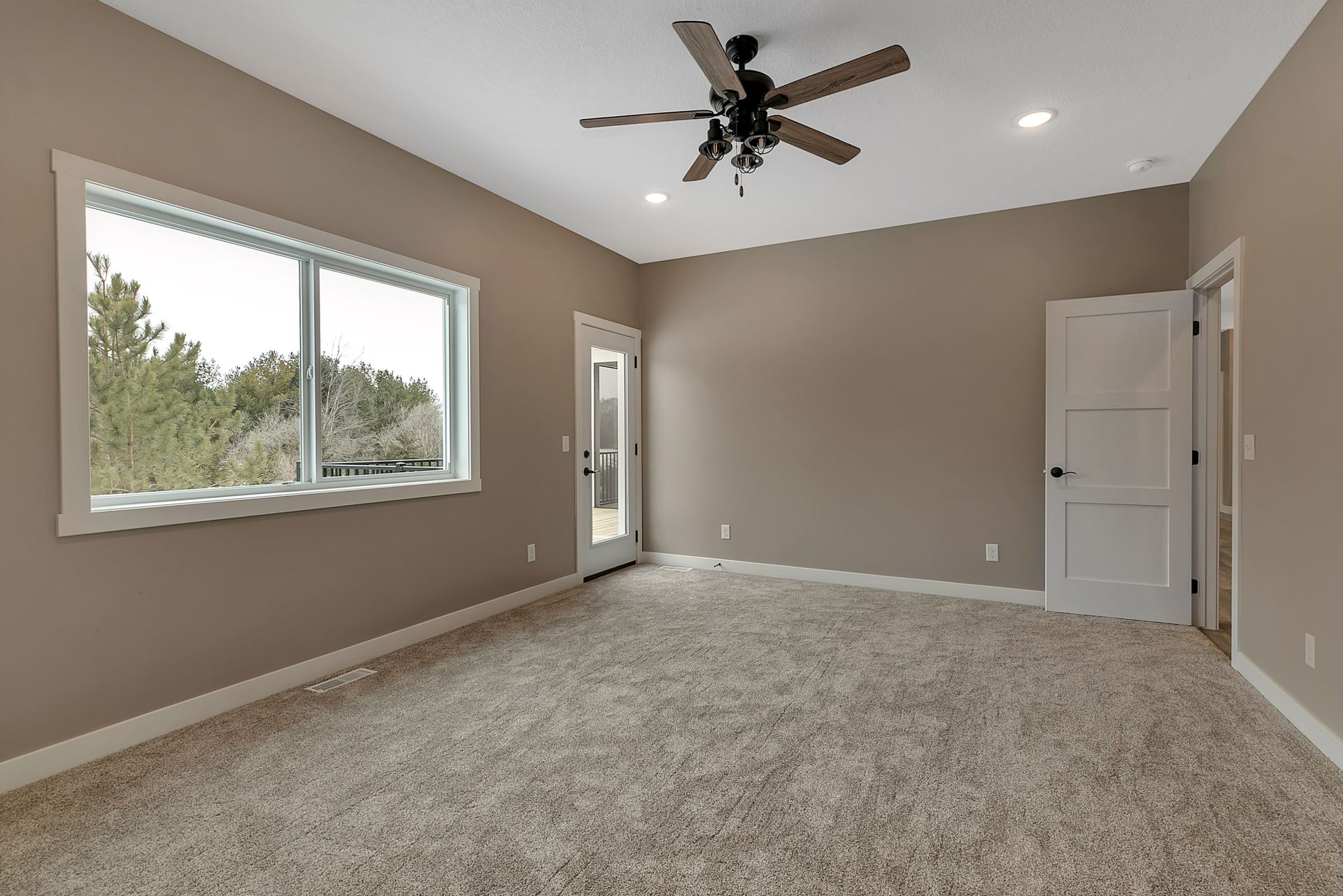 An empty room with a ceiling fan and two windows.