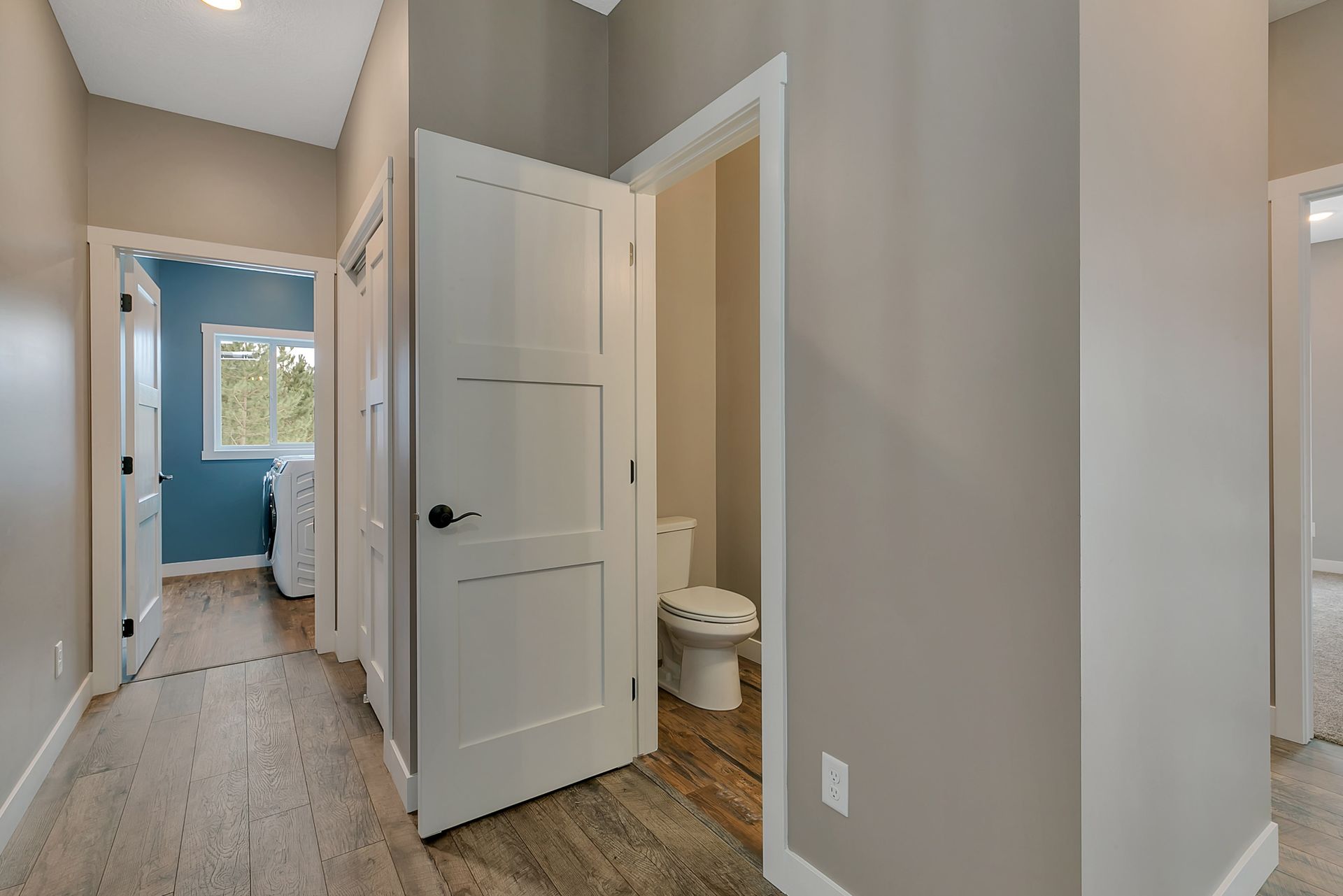 A hallway in a house with a toilet and a laundry room.