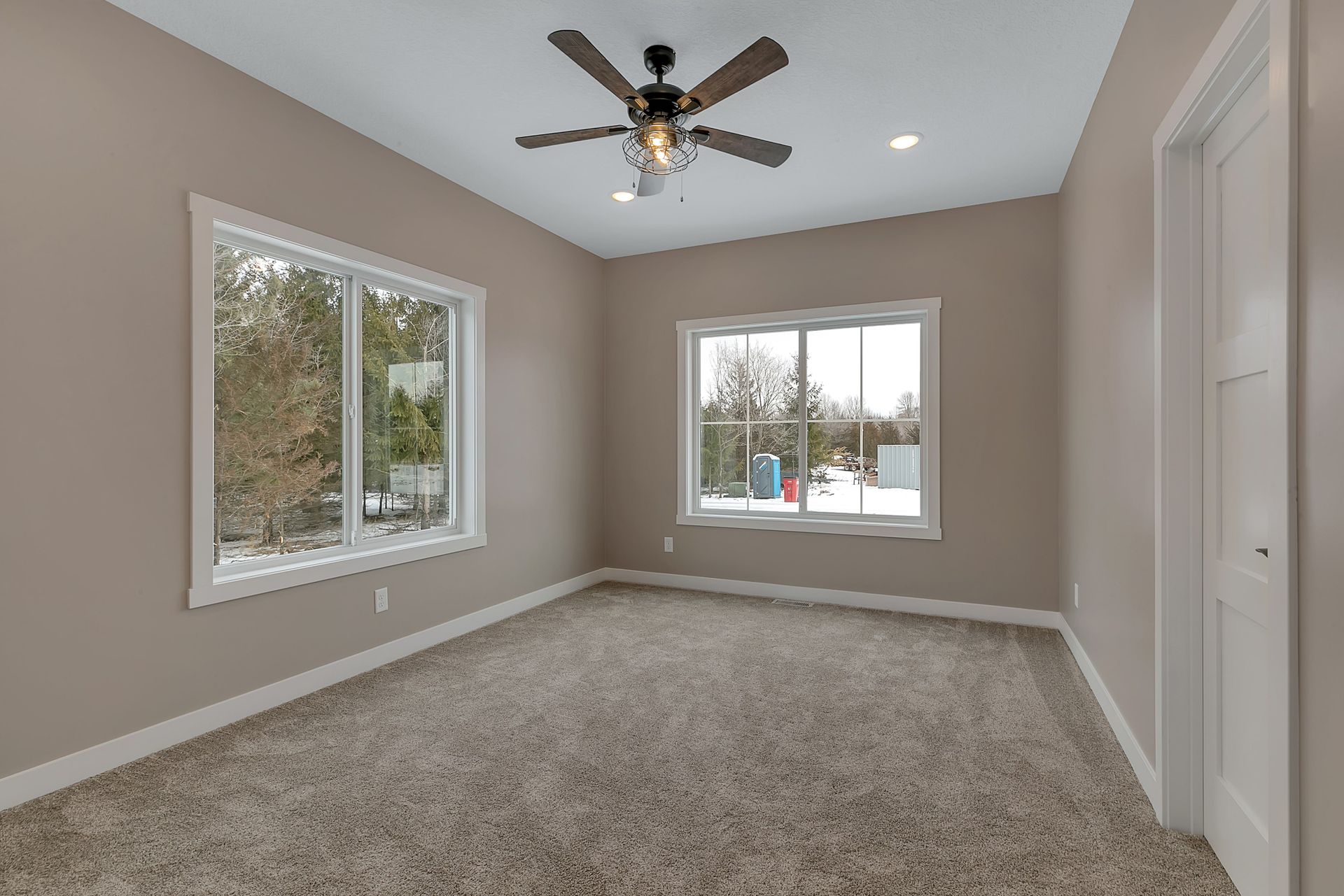 An empty bedroom with a ceiling fan and two windows.