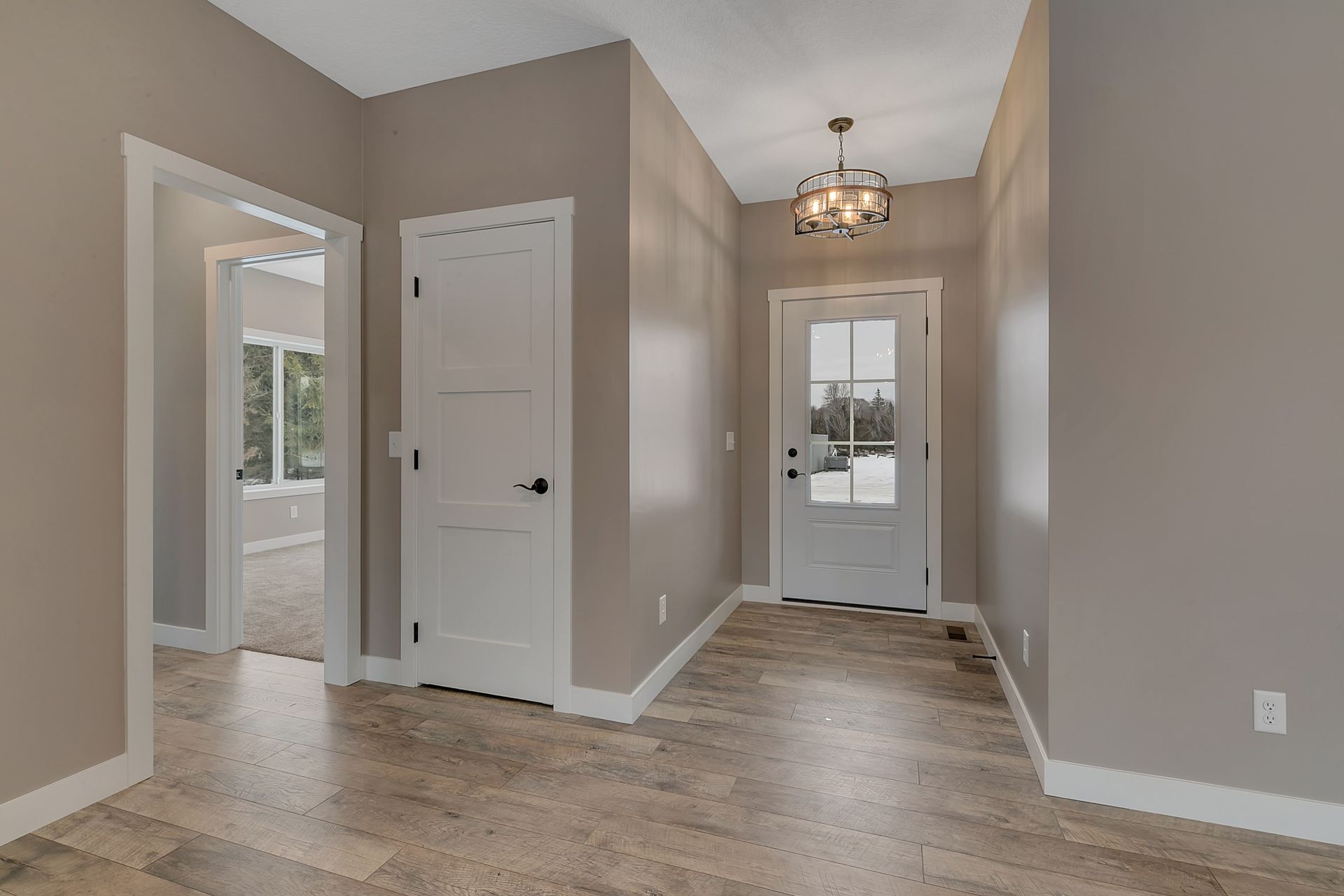 An empty hallway with a white door and a chandelier hanging from the ceiling.