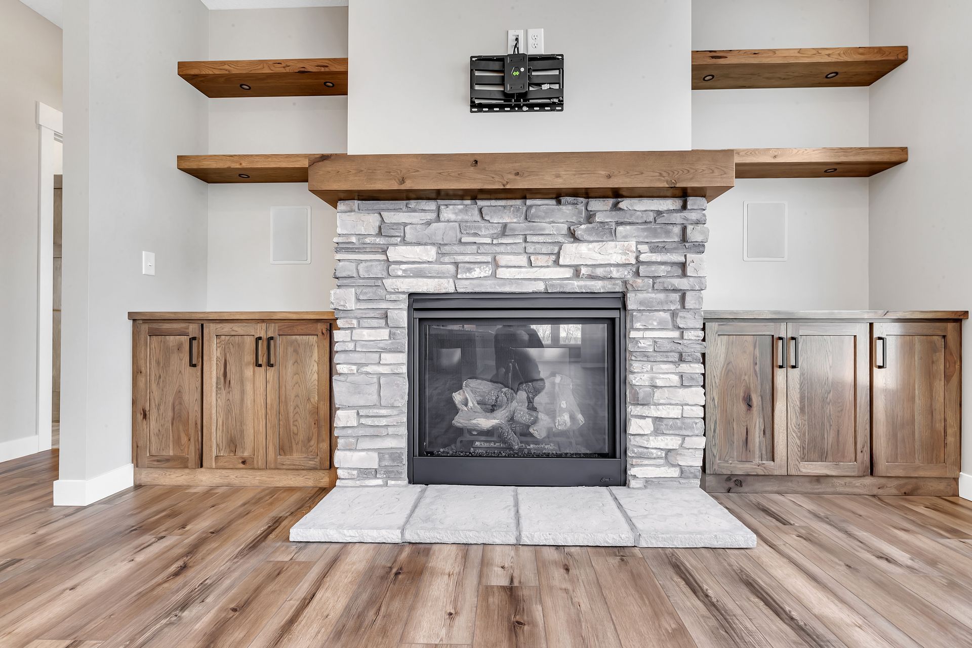 A living room with a stone fireplace and wooden shelves.