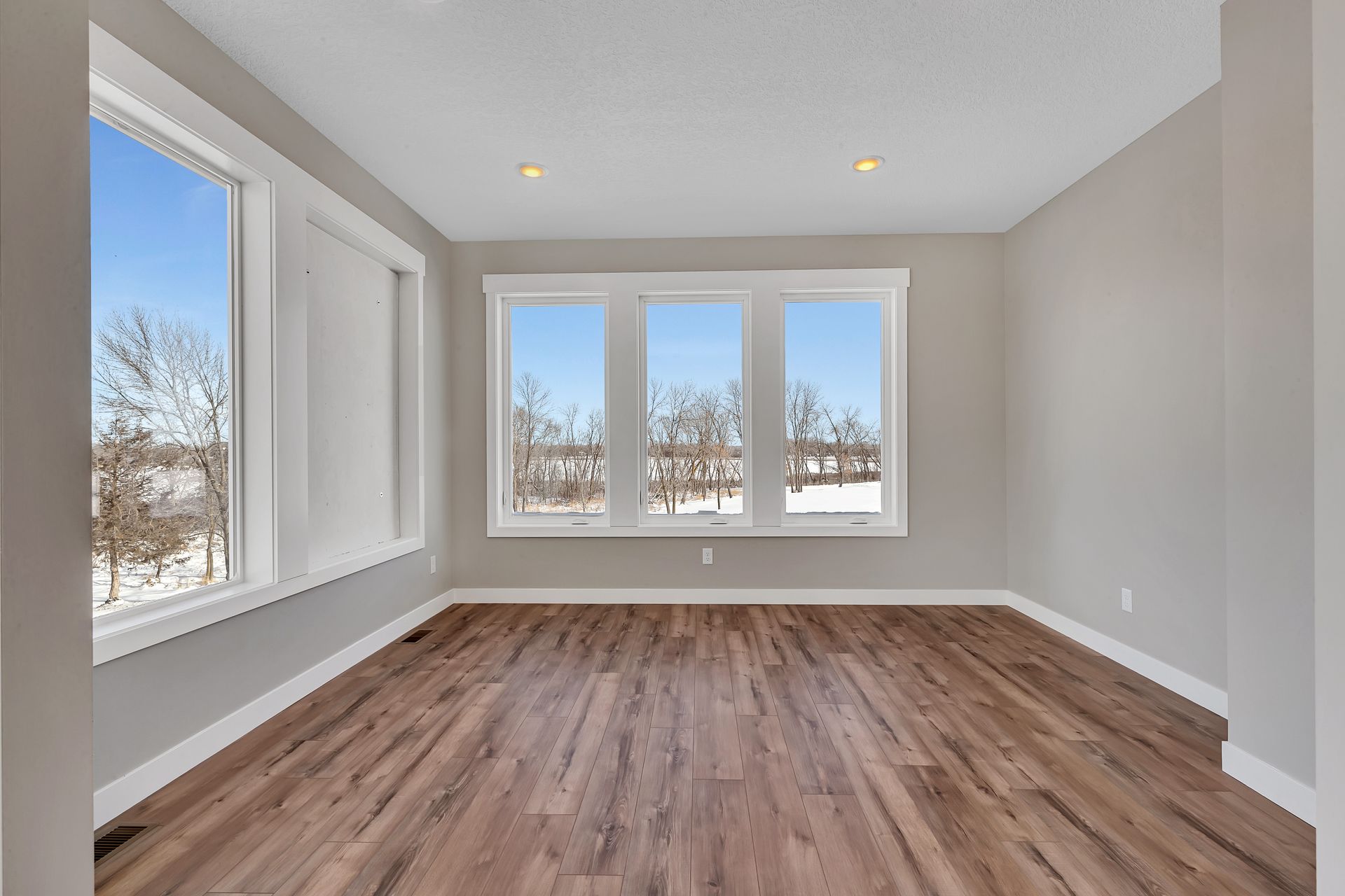 An empty living room with hardwood floors and three windows.