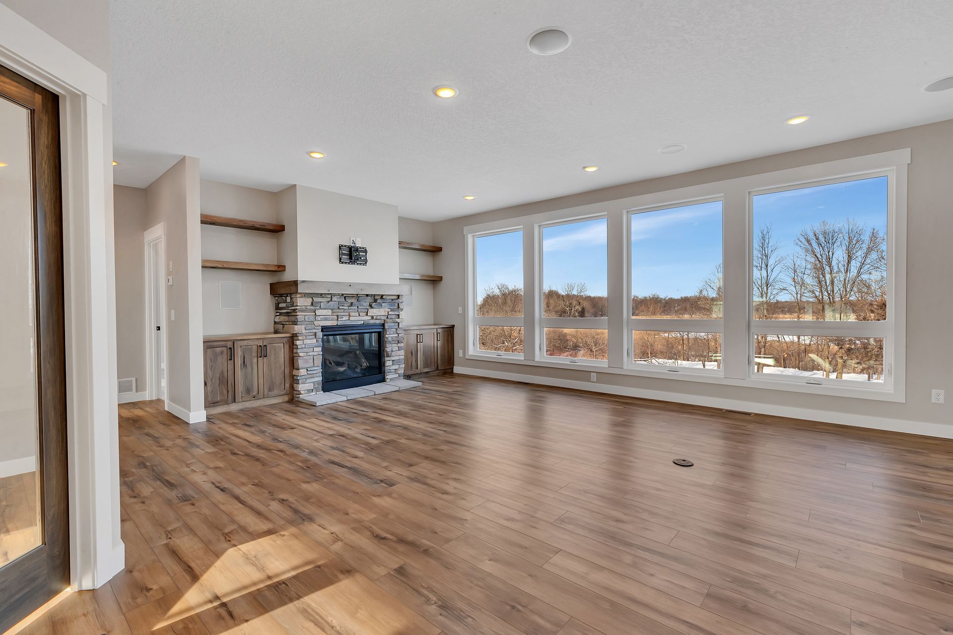 An empty living room with hardwood floors , a fireplace , and lots of windows.