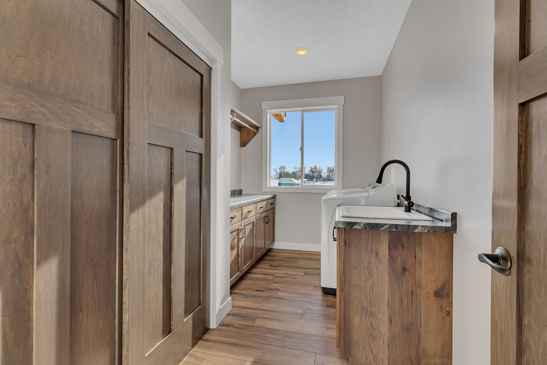 A laundry room with wooden cabinets , a sink , and a window.