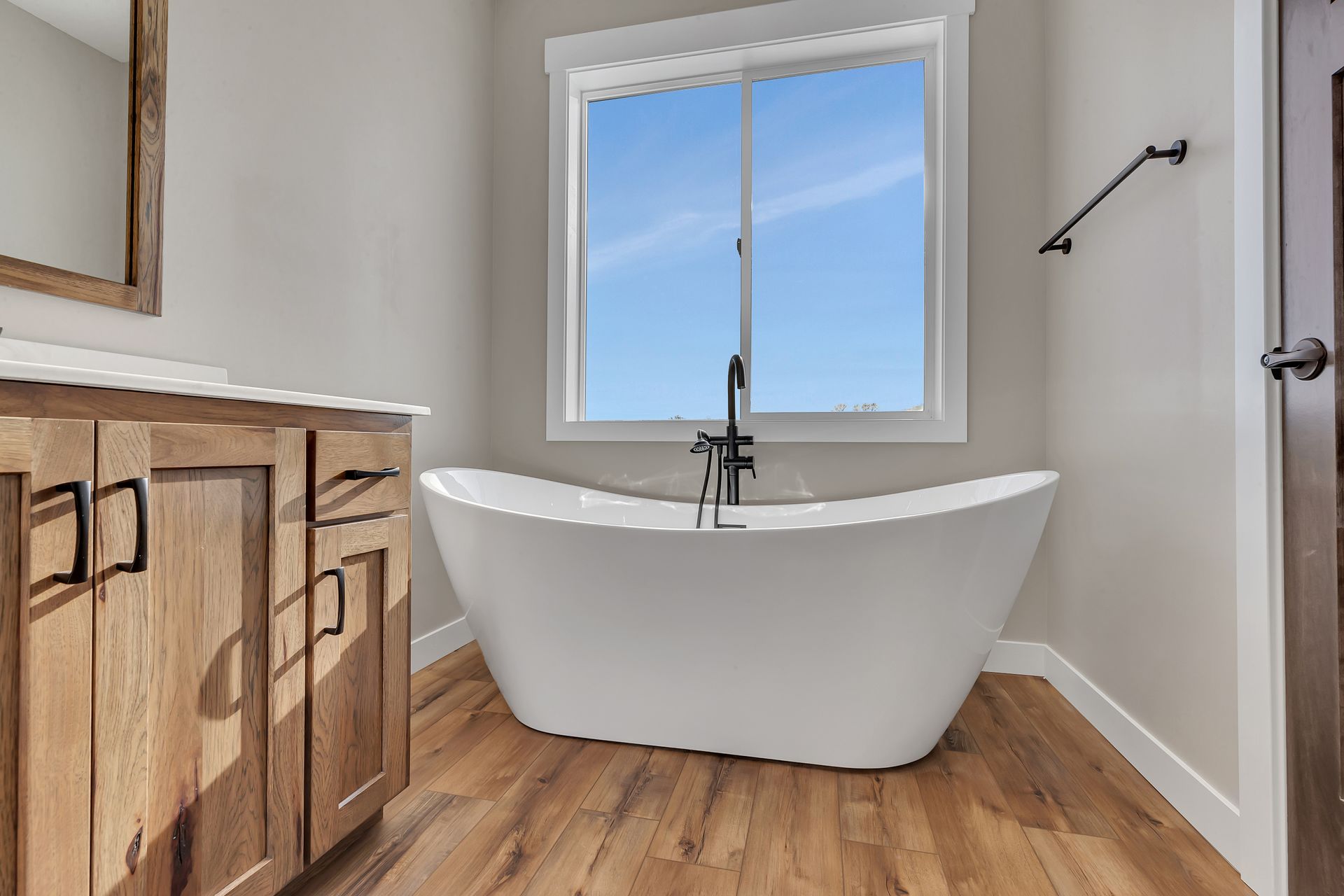 A bathroom with a tub , sink , mirror and window.