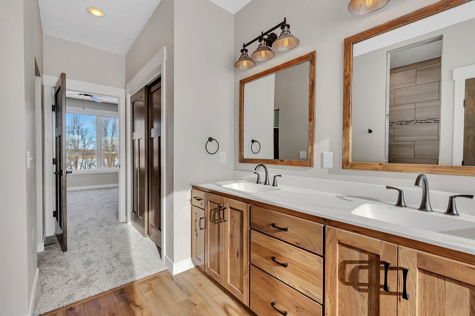 A bathroom with two sinks , two mirrors , and wooden cabinets.