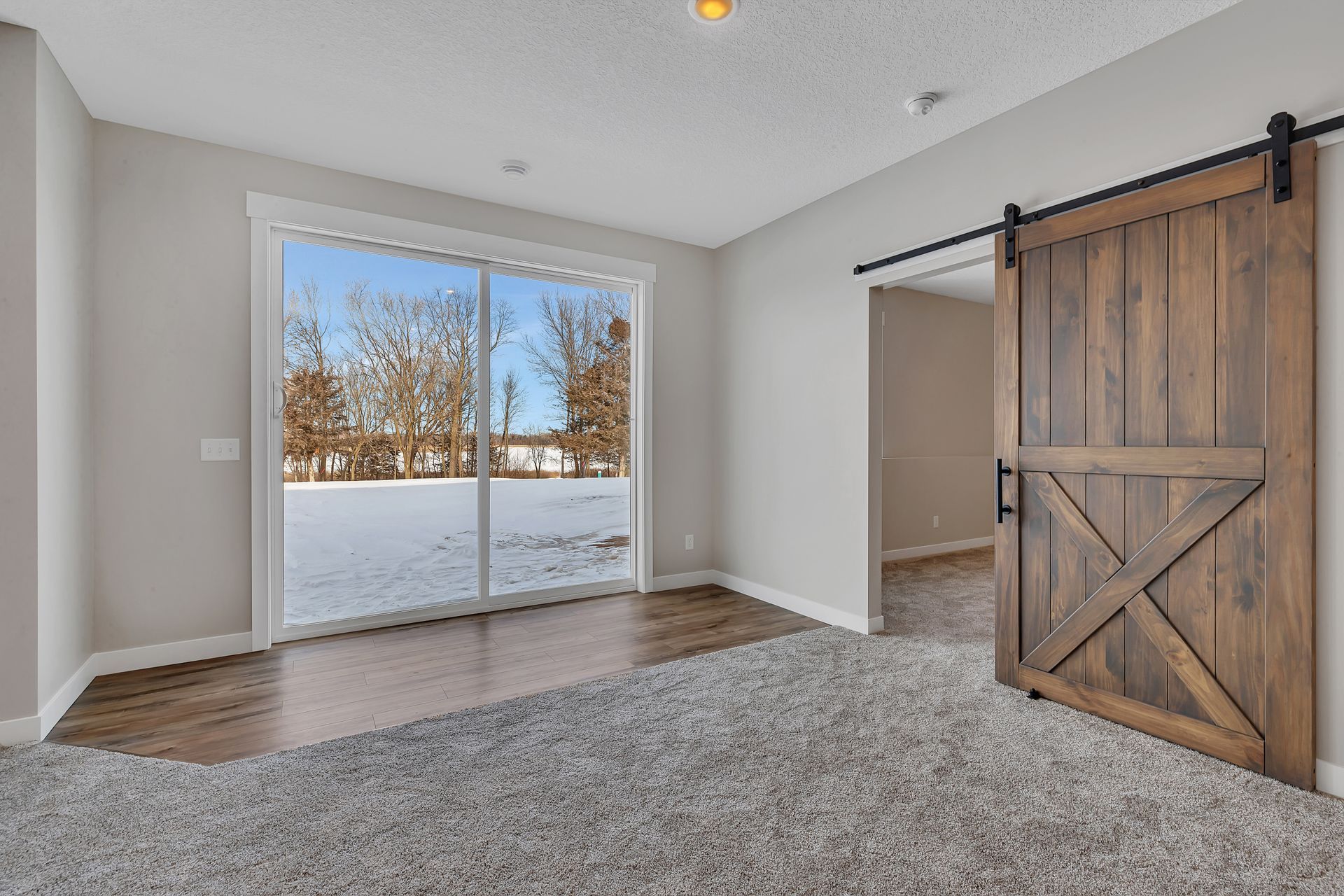 An empty room with a sliding glass door and a wooden barn door.