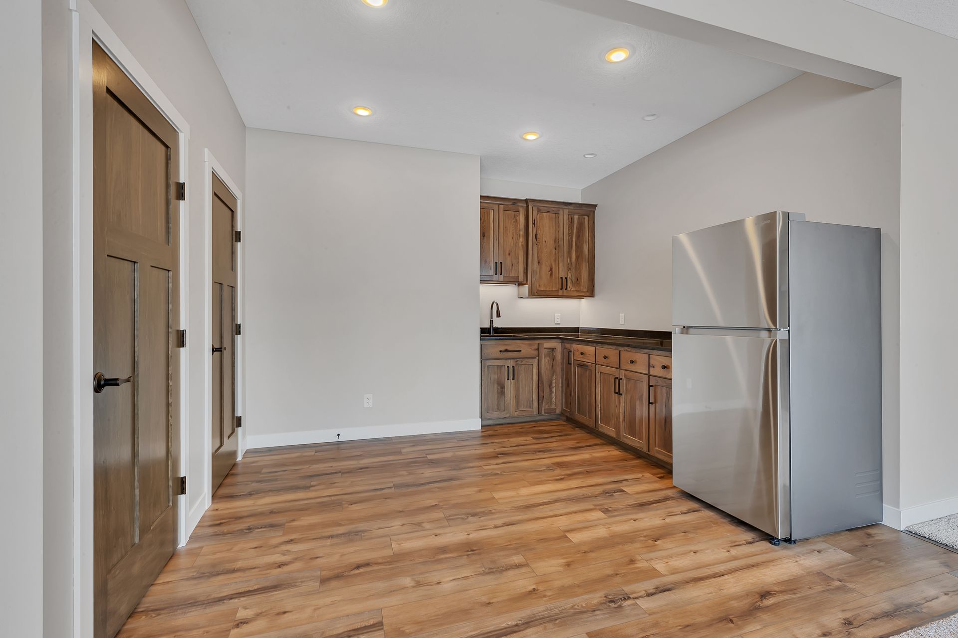 An empty kitchen with wooden floors and a stainless steel refrigerator.