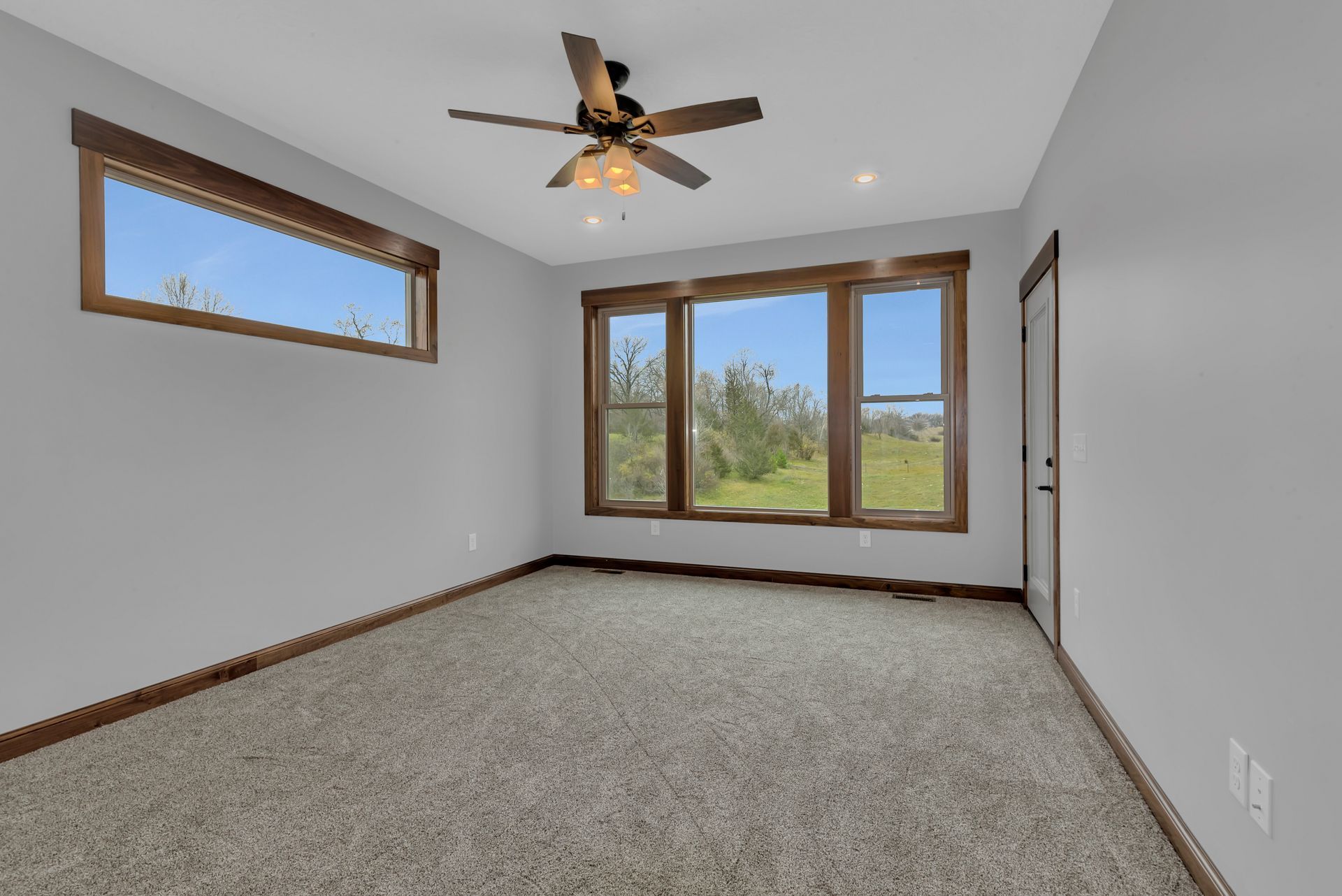 An empty room with a ceiling fan and three windows.
