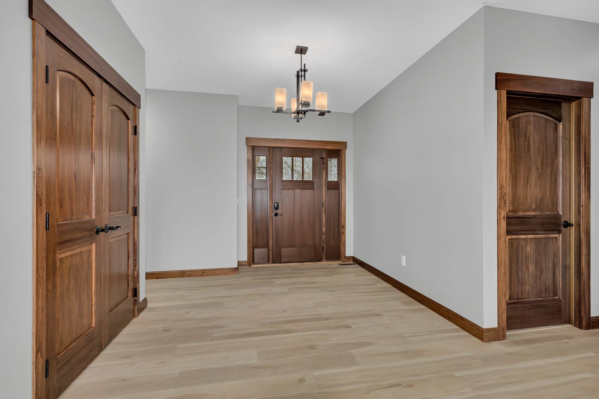 An empty hallway with wooden doors and a chandelier hanging from the ceiling.