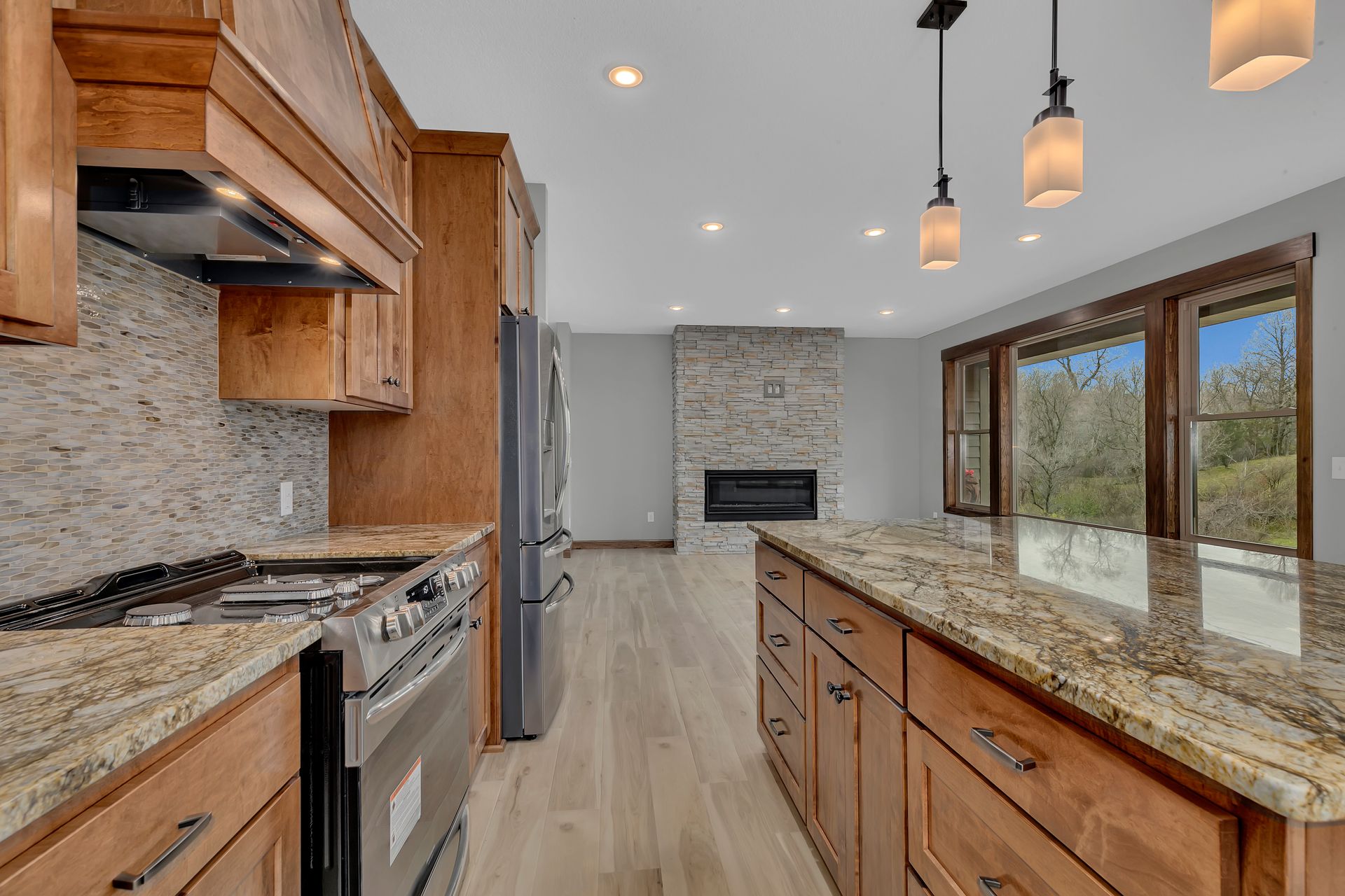 A kitchen with granite counter tops , wooden cabinets , stainless steel appliances and a fireplace.