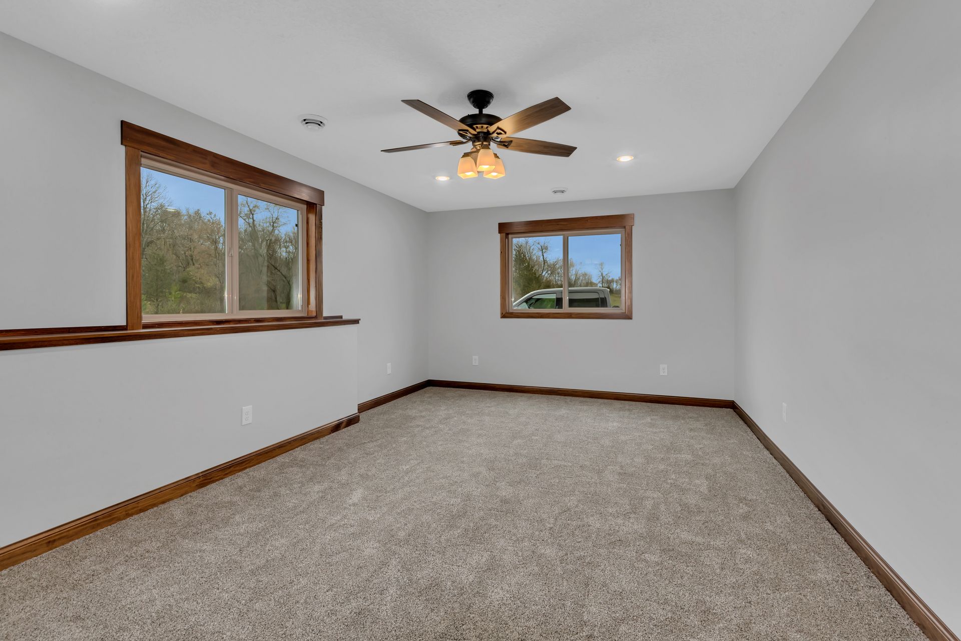 An empty room with a ceiling fan and two windows.