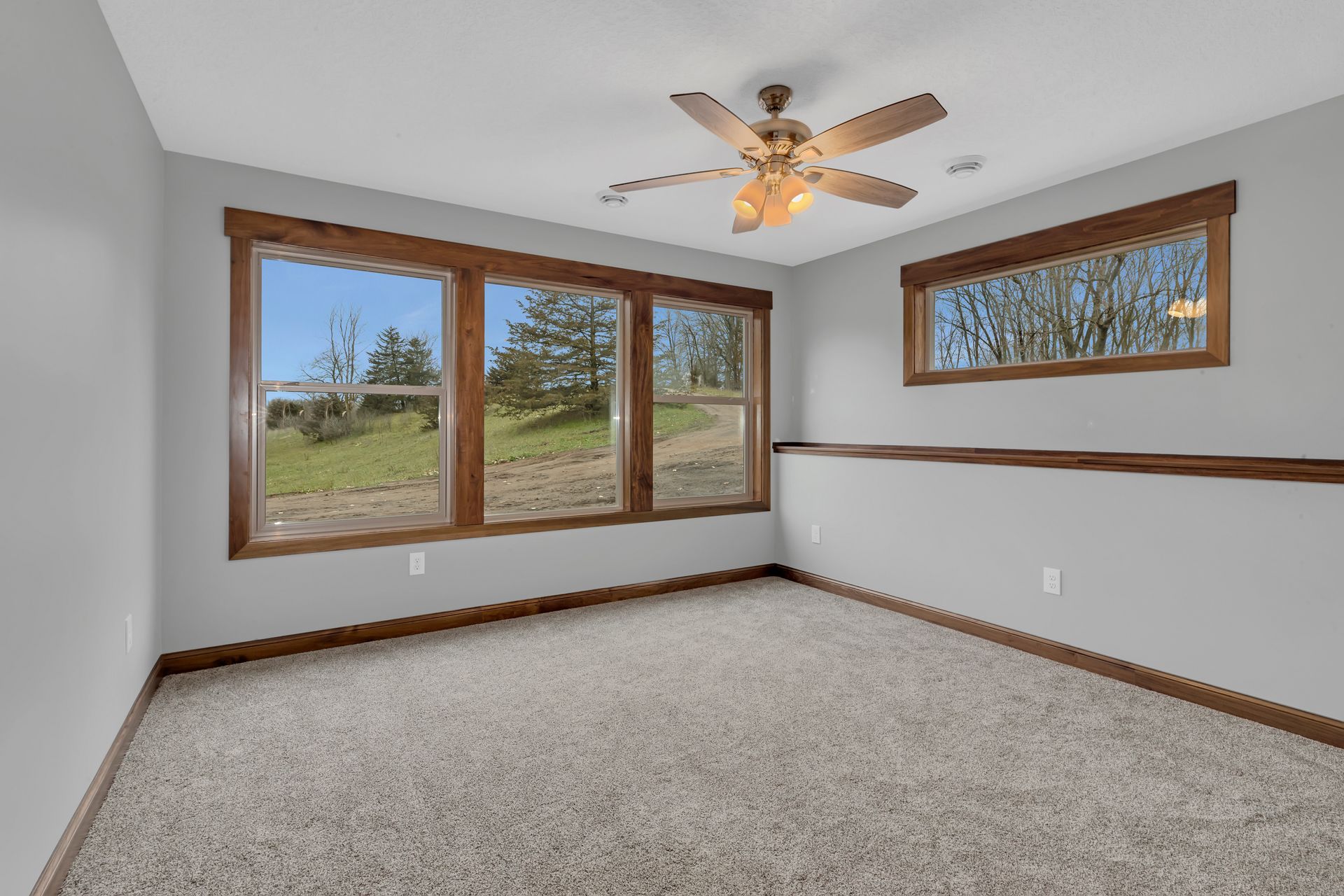 An empty room with a ceiling fan and three windows.