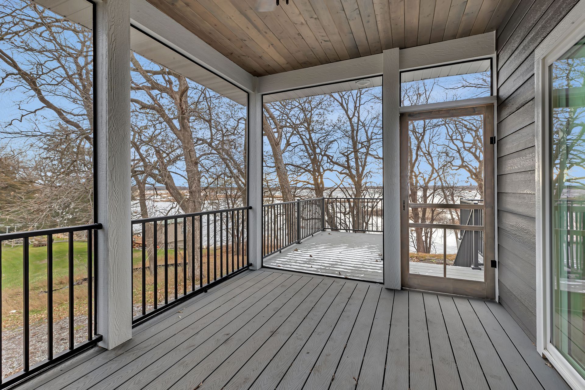 A screened in porch with a view of trees and a lake.