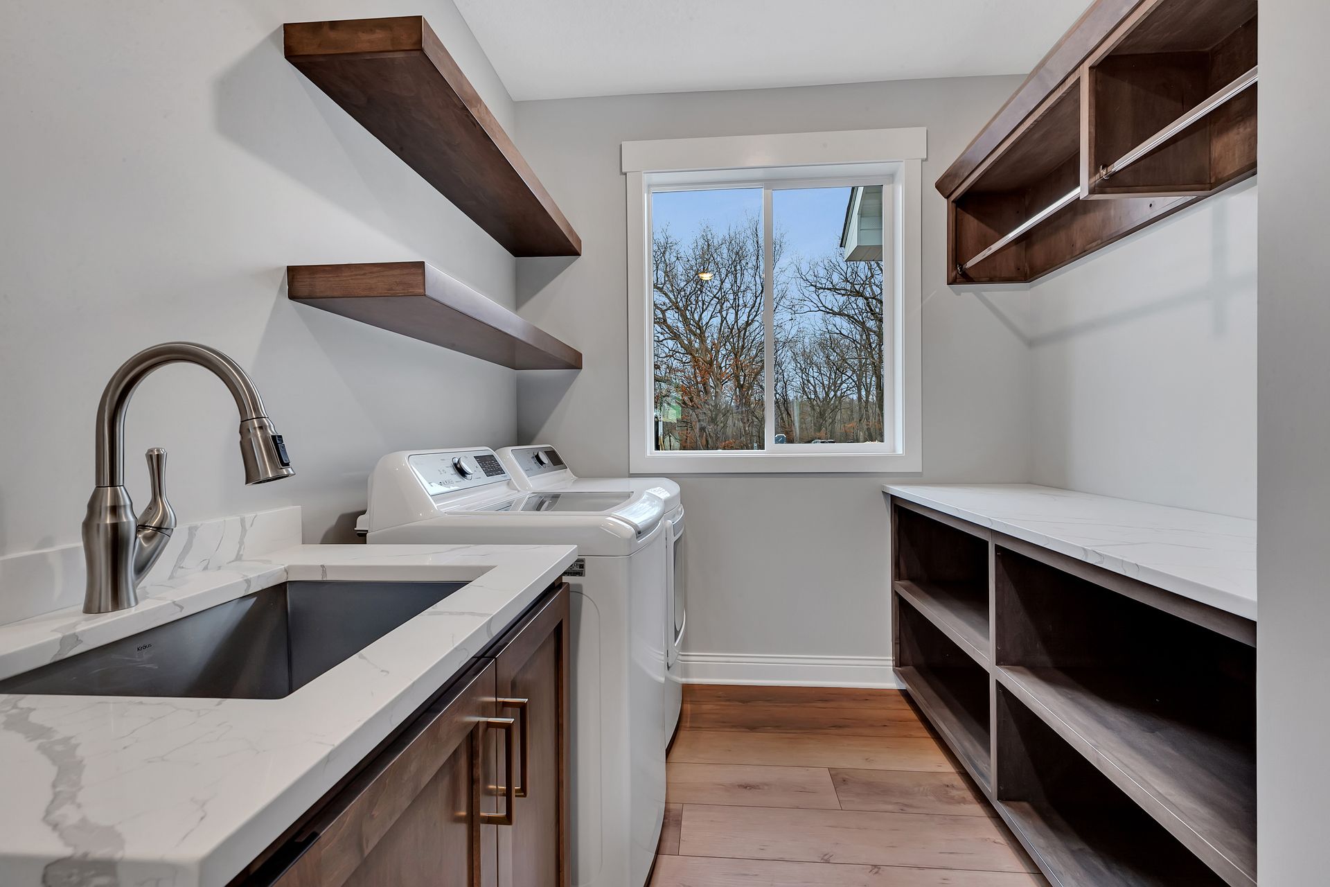 A laundry room with a sink , washer and dryer , and shelves.