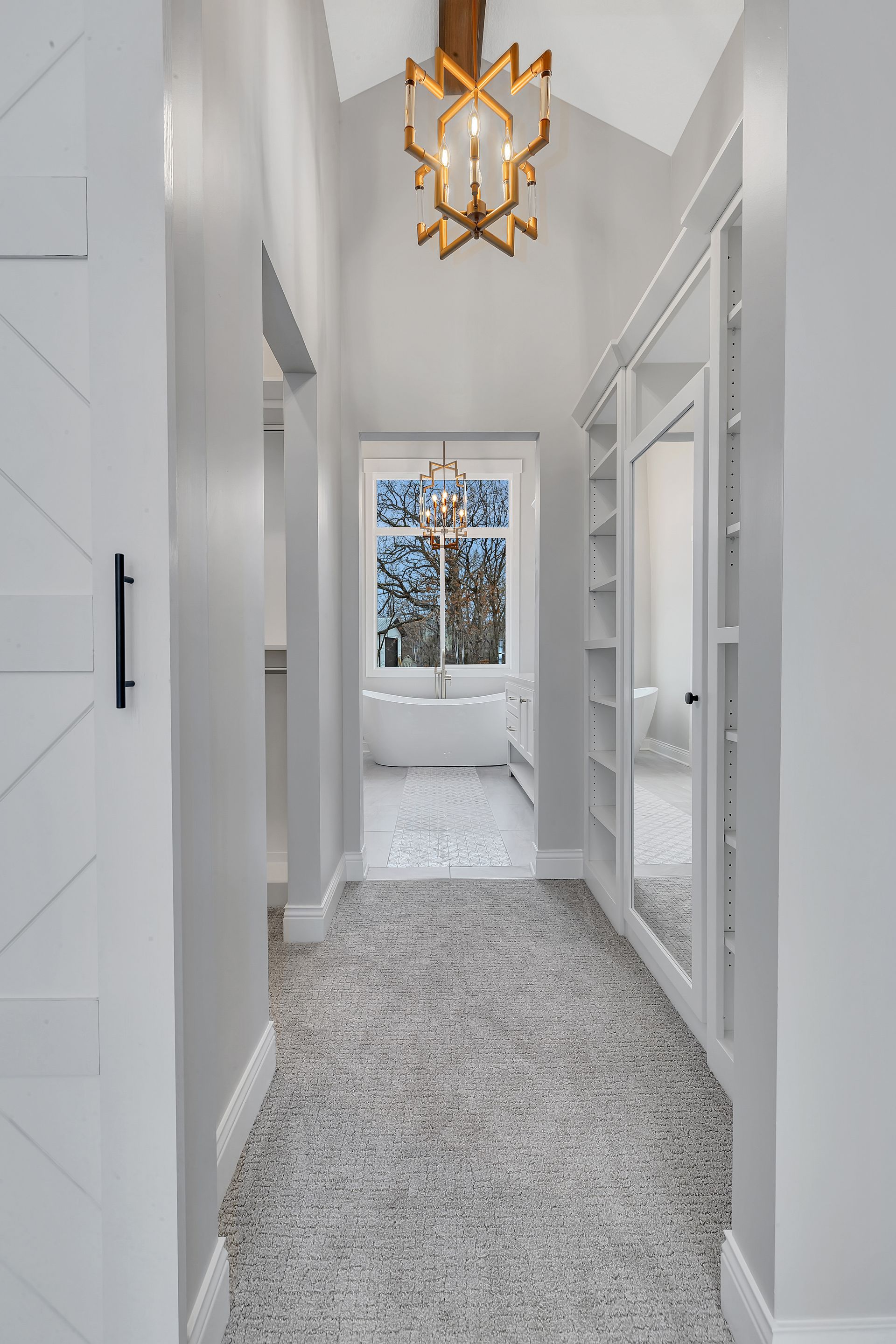 A long hallway leading to a bathroom with a chandelier hanging from the ceiling.