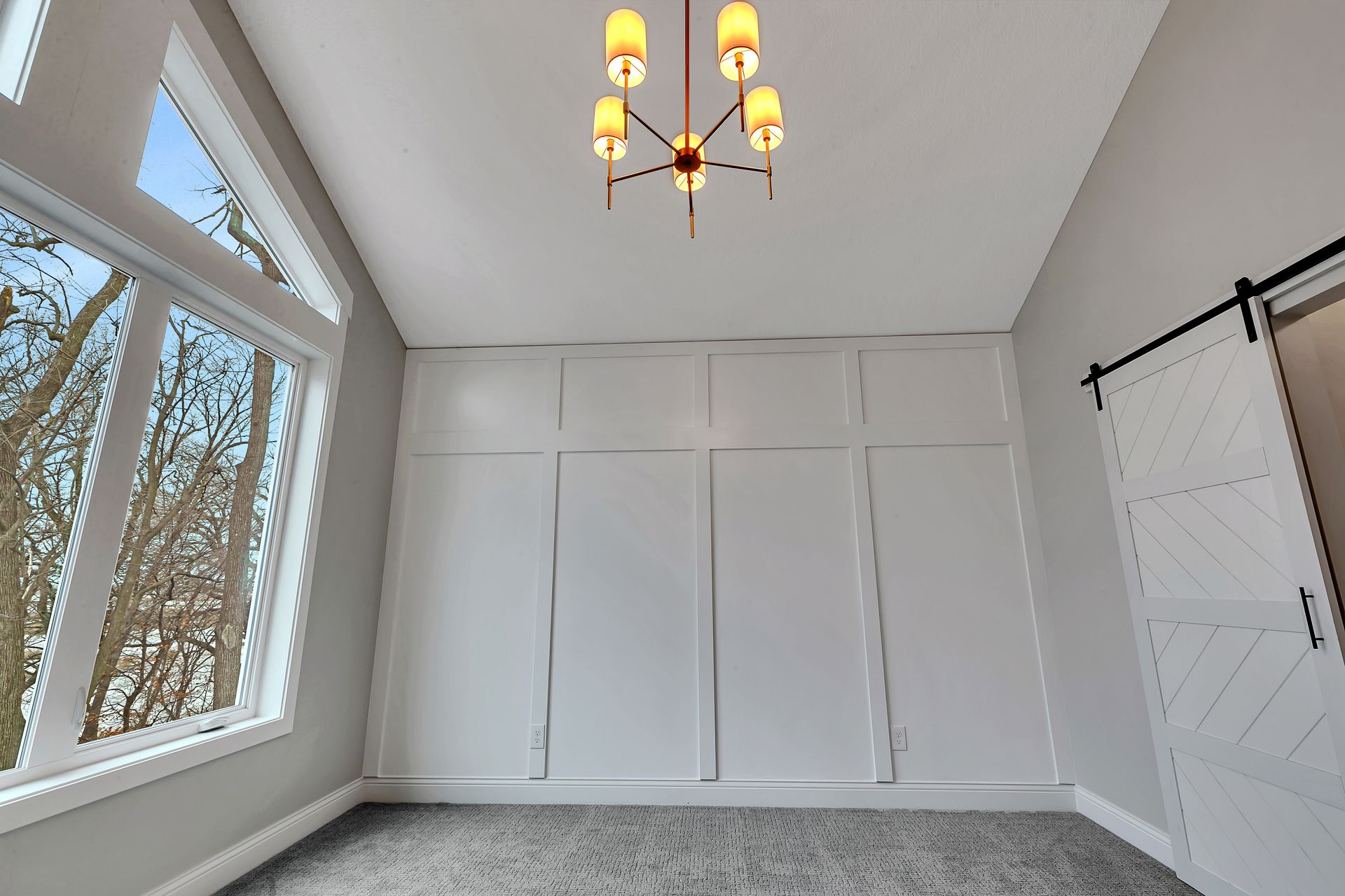 An empty room with a chandelier hanging from the ceiling and a sliding barn door.