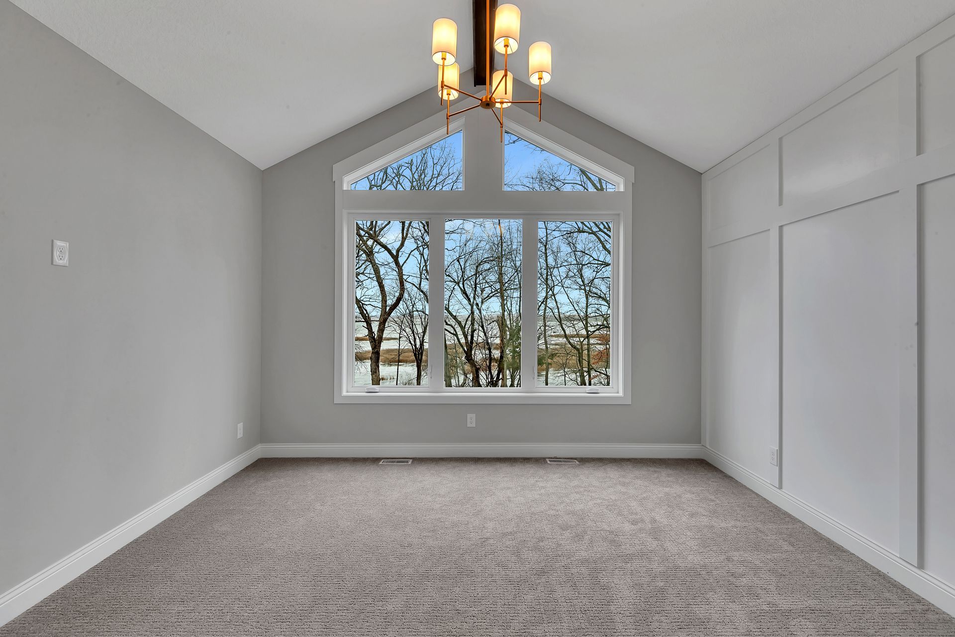 An empty room with a large window and a chandelier.