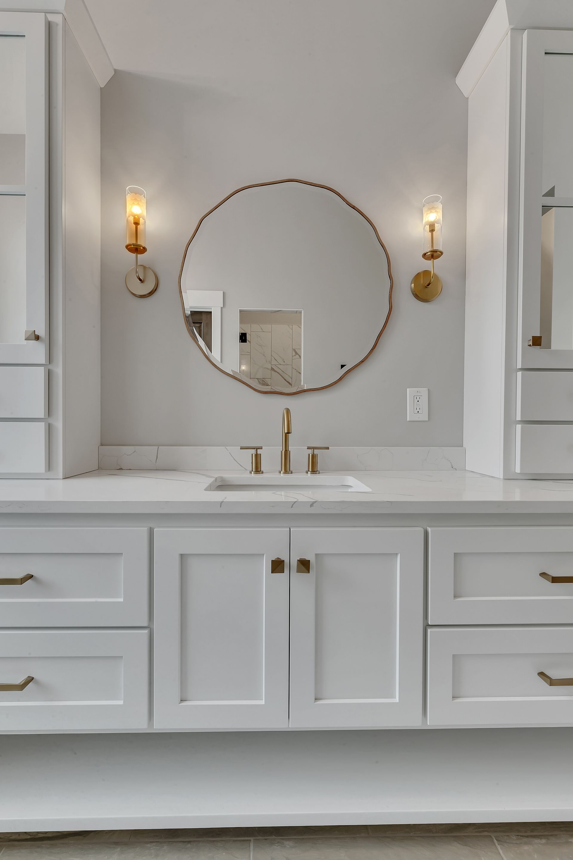 A bathroom with white cabinets , a sink , and a round mirror.
