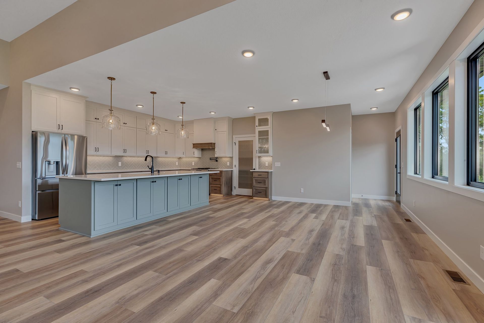 A large empty room with hardwood floors and a kitchen in the background.