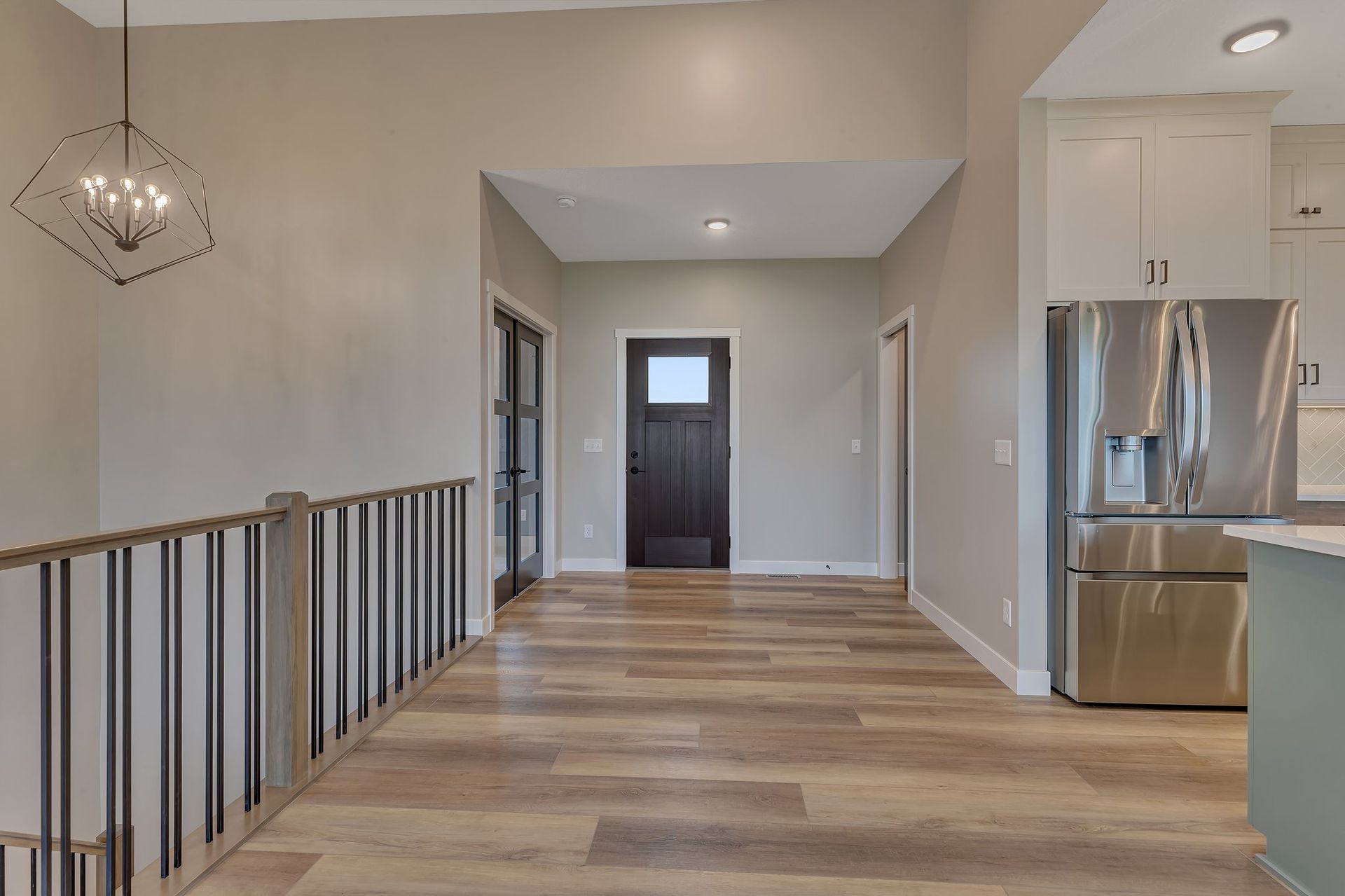 A hallway in a house with hardwood floors and a stainless steel refrigerator.