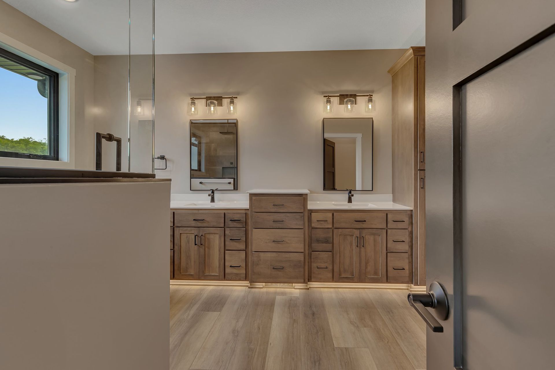 A bathroom with two sinks , two mirrors , and hardwood floors.