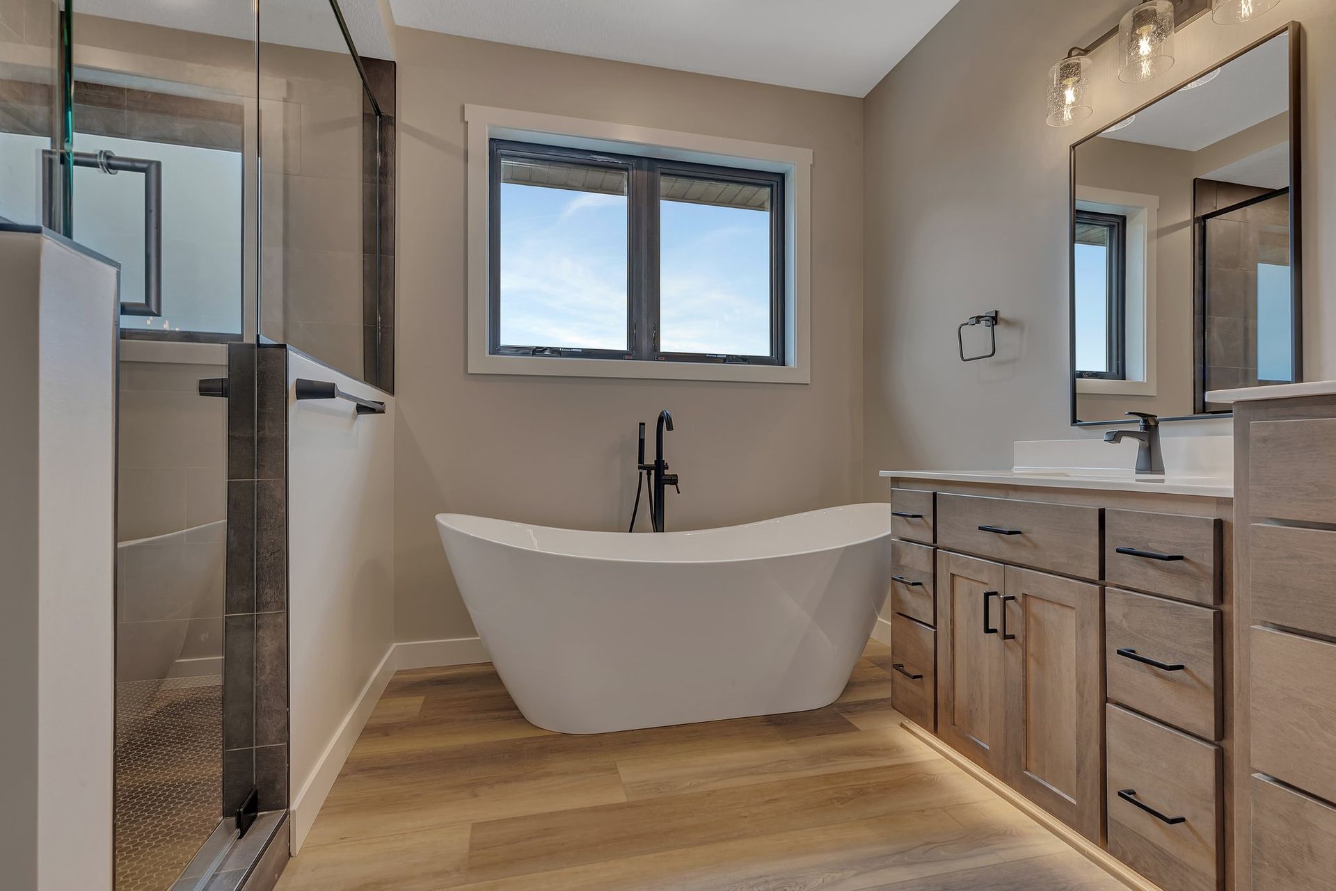 A bathroom with a tub , sink , mirror and window.