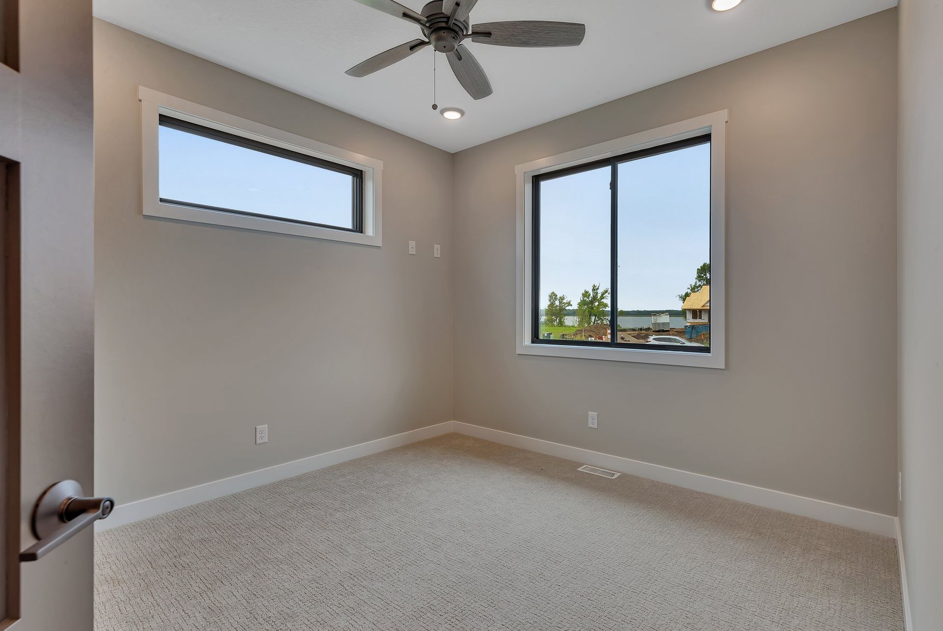 An empty bedroom with a ceiling fan and two windows.