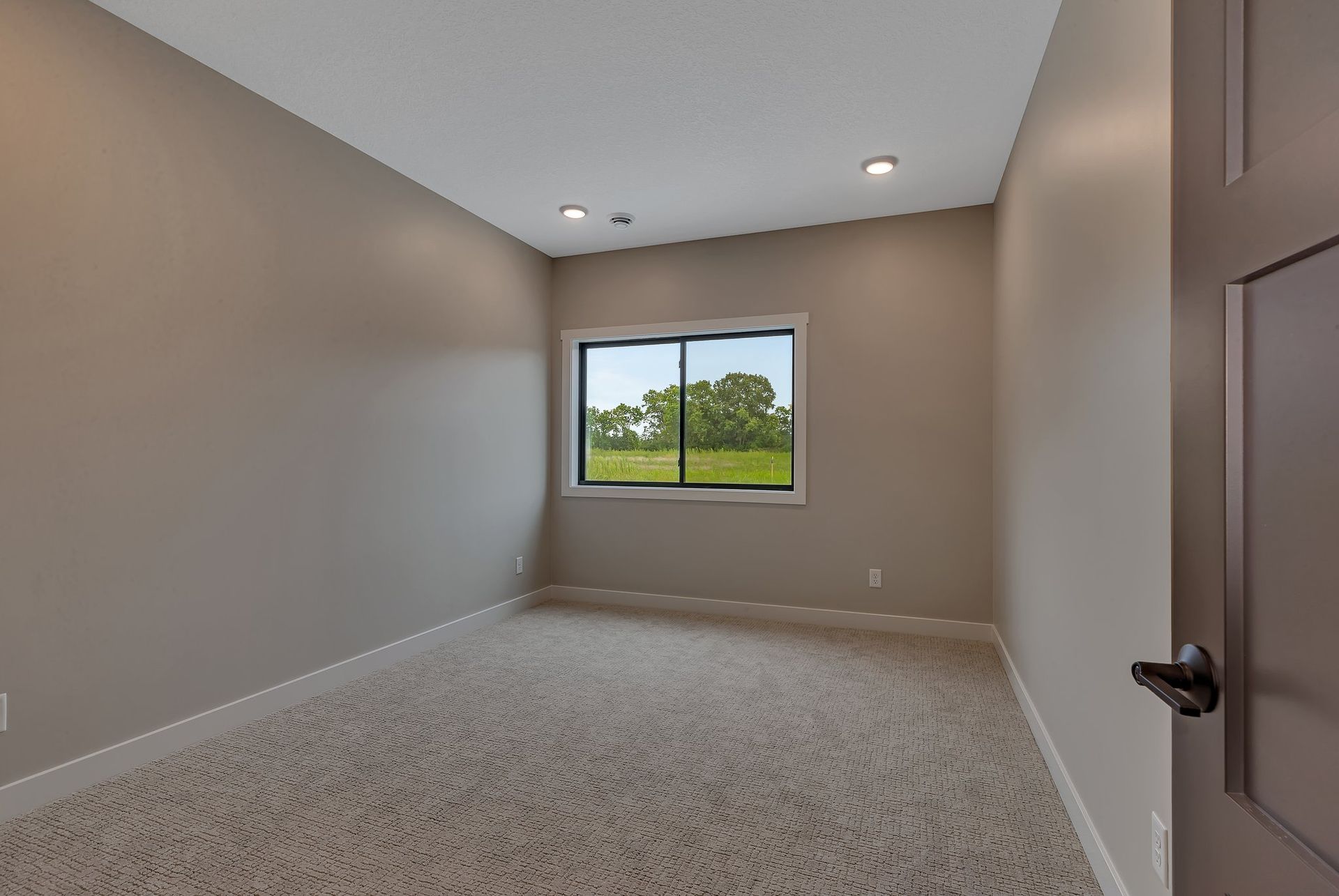 An empty bedroom with a large window and a carpeted floor.