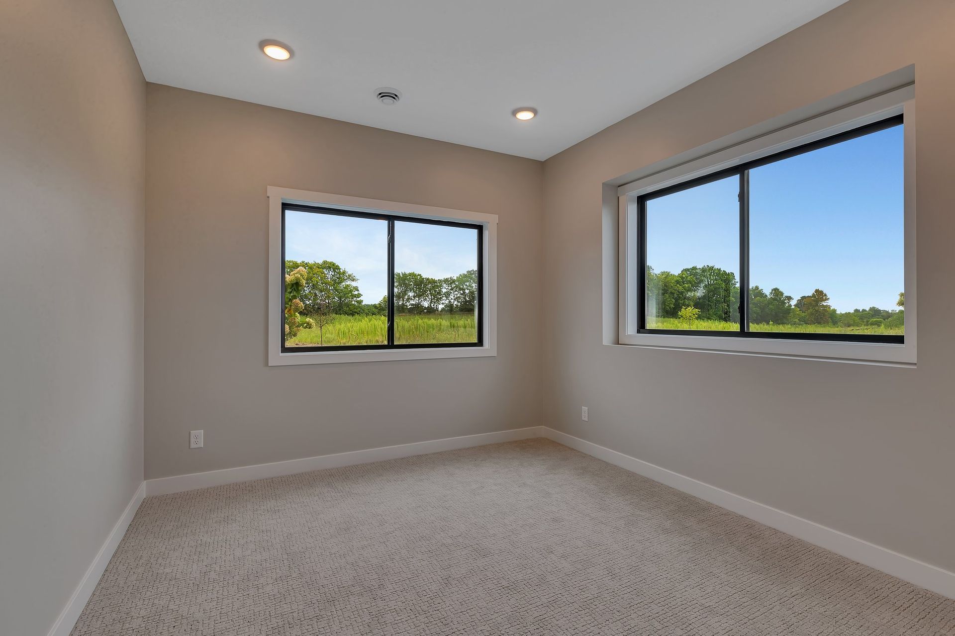 An empty room with two windows and a carpeted floor.