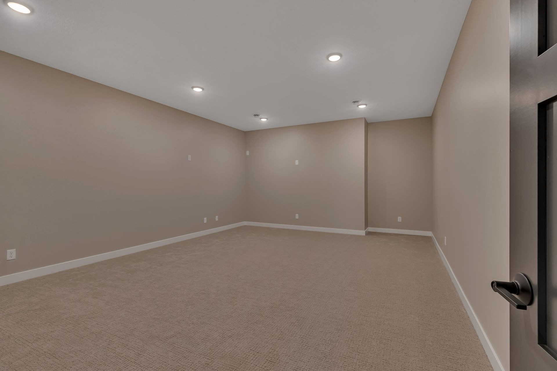 An empty basement with a carpeted floor and beige walls.