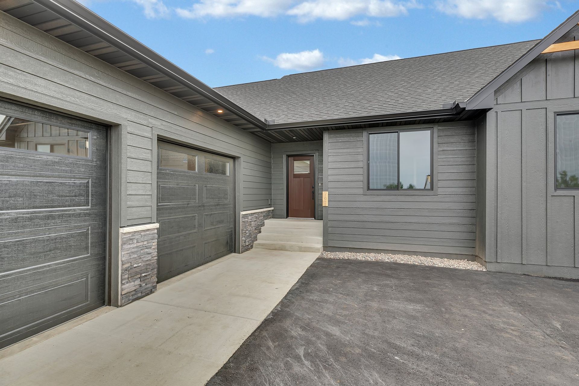 A gray house with two garage doors and a concrete walkway leading to the front door.
