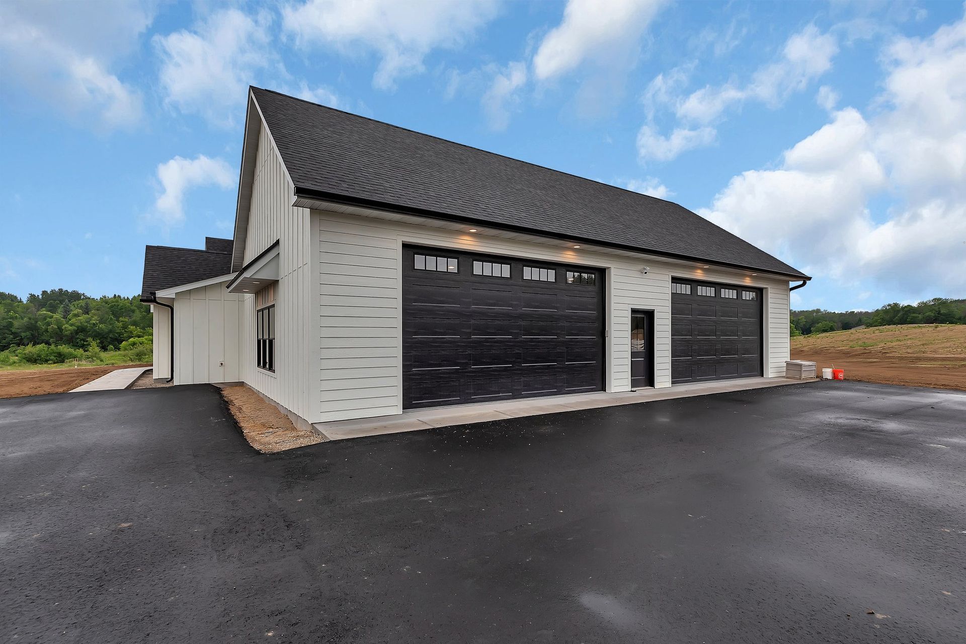 Modern detached garage with black doors and a paved driveway under a cloudy sky