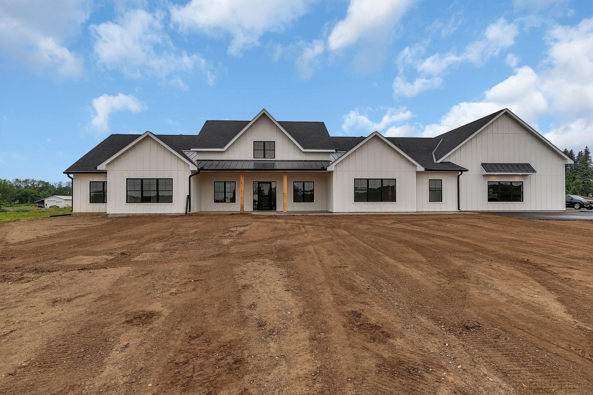 A large white house is sitting in the middle of a dirt field.