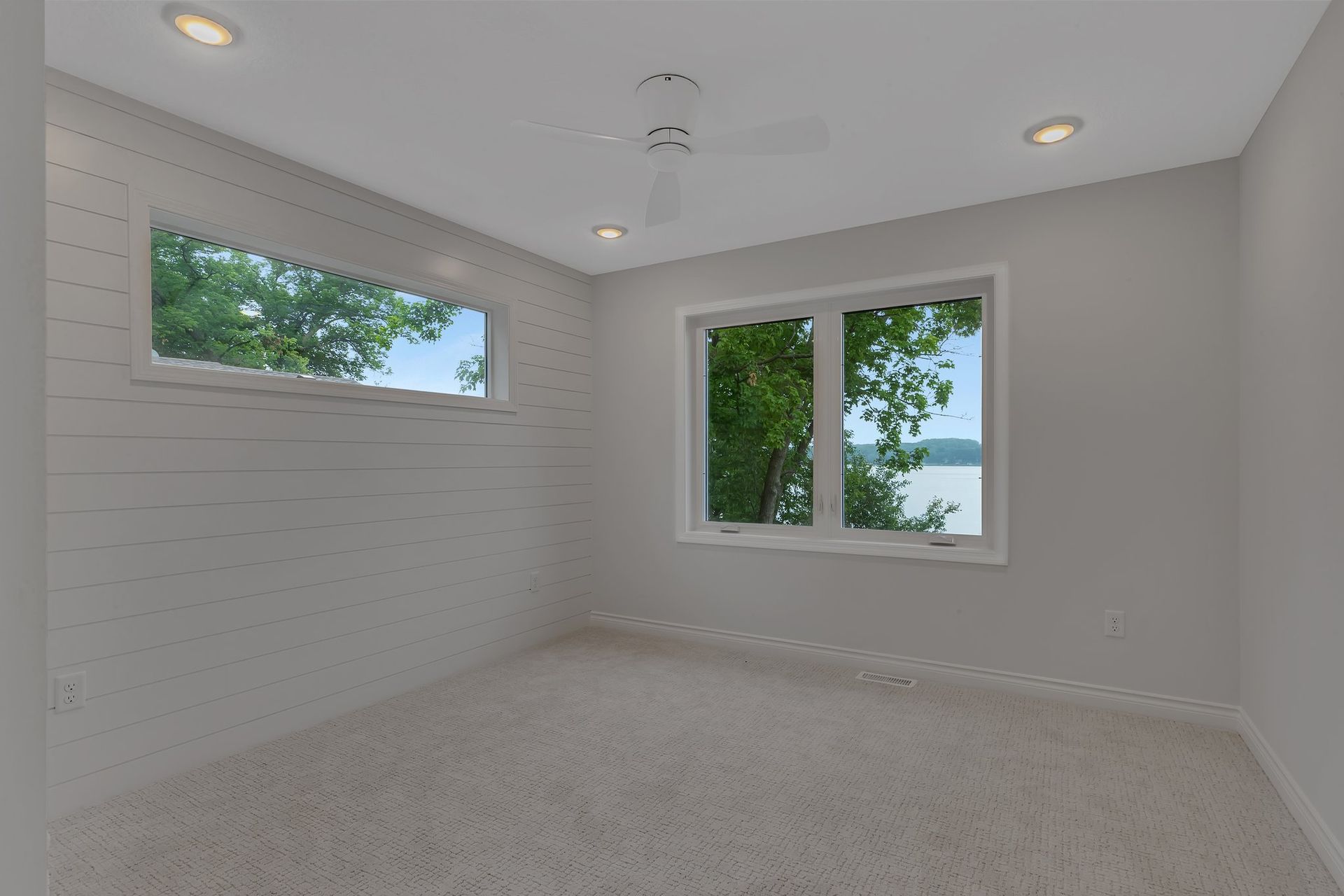 An empty room with two windows and a ceiling fan.