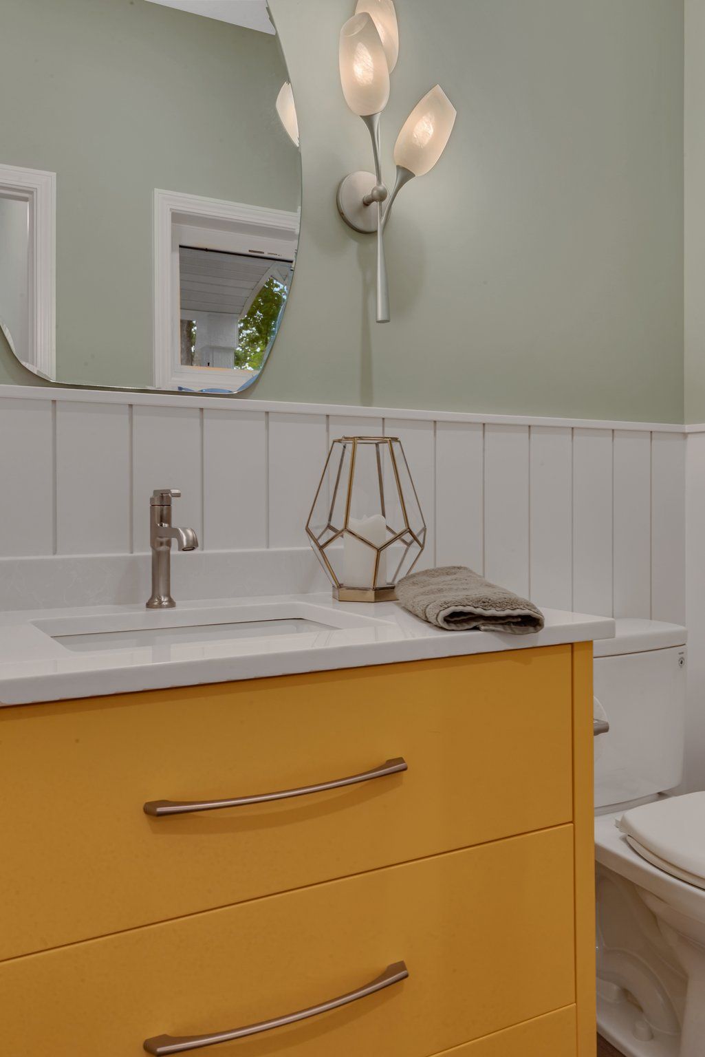 A bathroom with a sink , toilet , mirror and yellow cabinets.