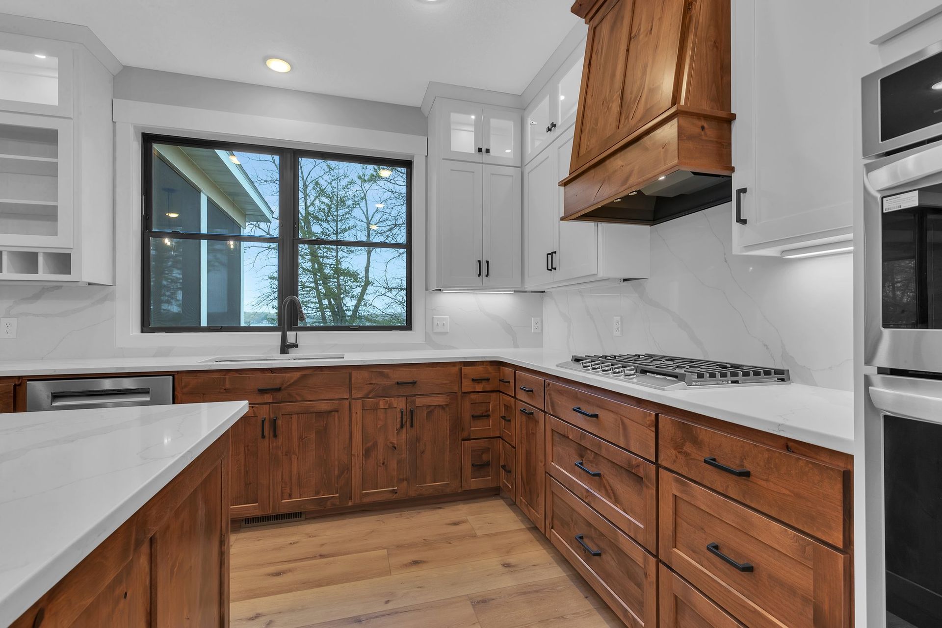 A kitchen with wooden cabinets , white counter tops , stainless steel appliances and a large window.