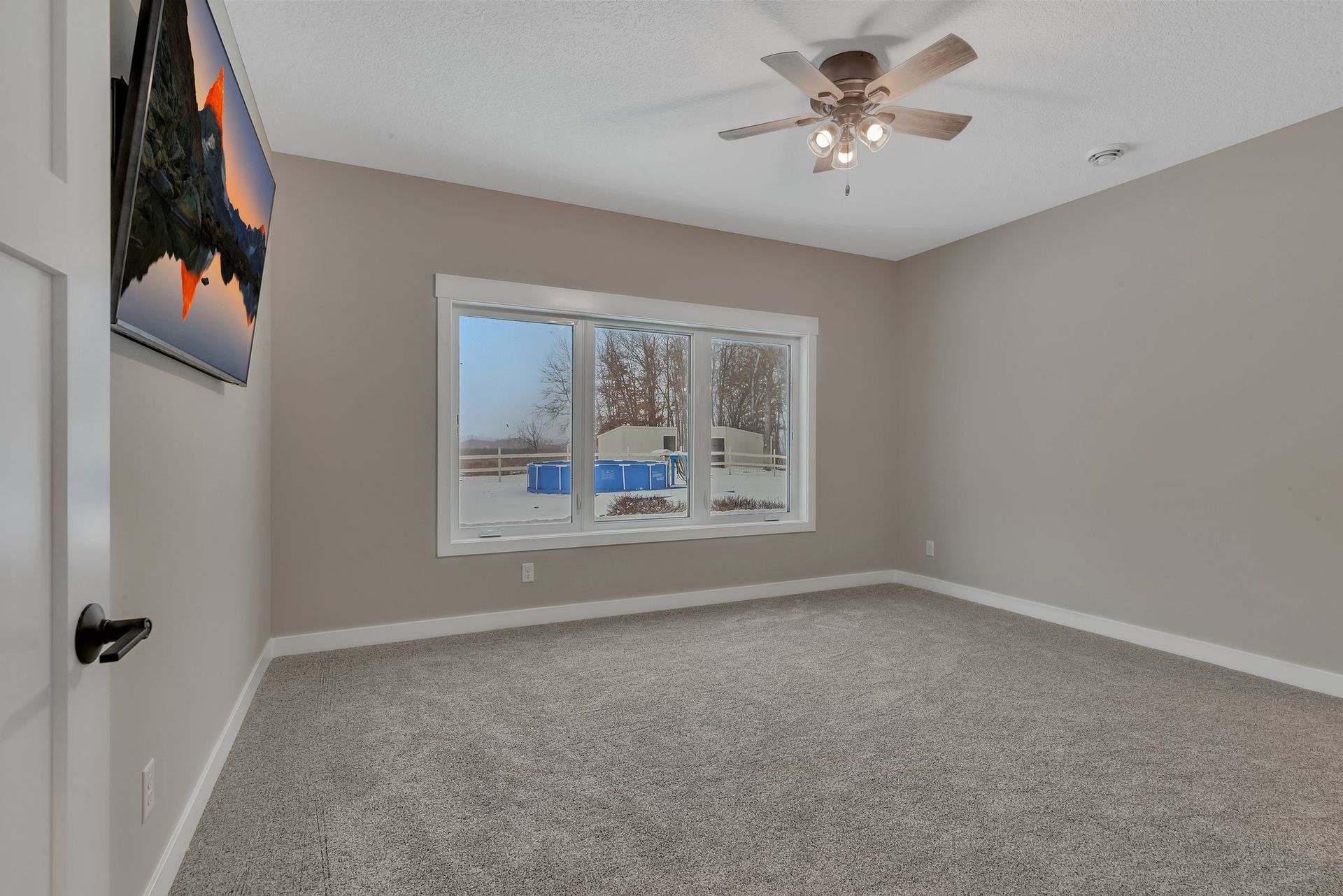 An empty bedroom with a ceiling fan and a television on the wall.