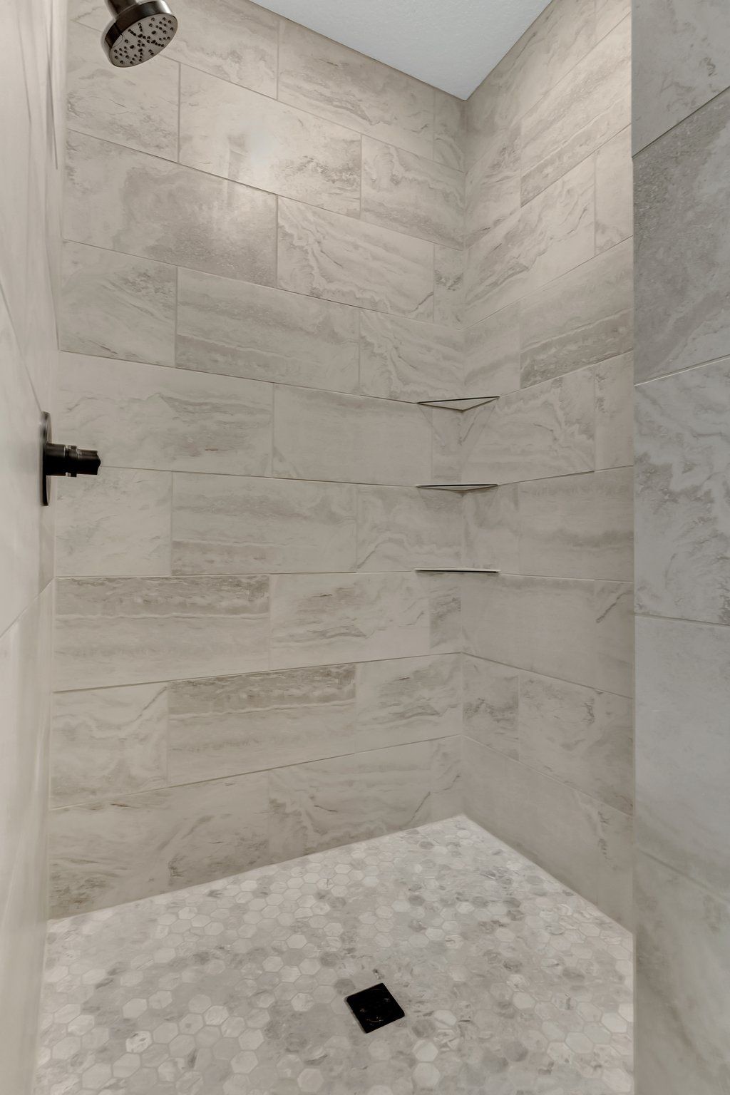 A walk in shower with a shower head and shelves in a bathroom.