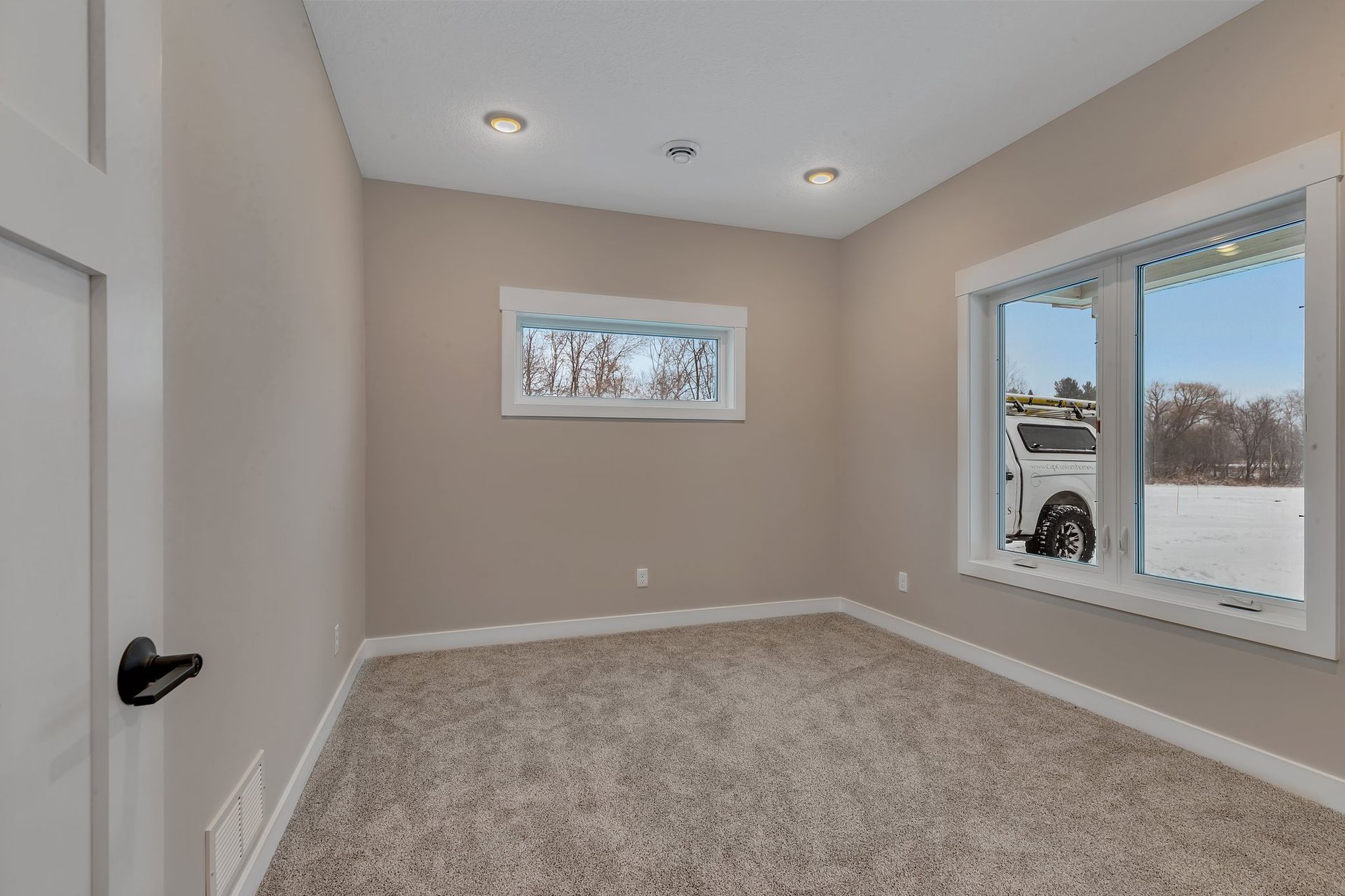 An empty room with a carpeted floor and two windows.