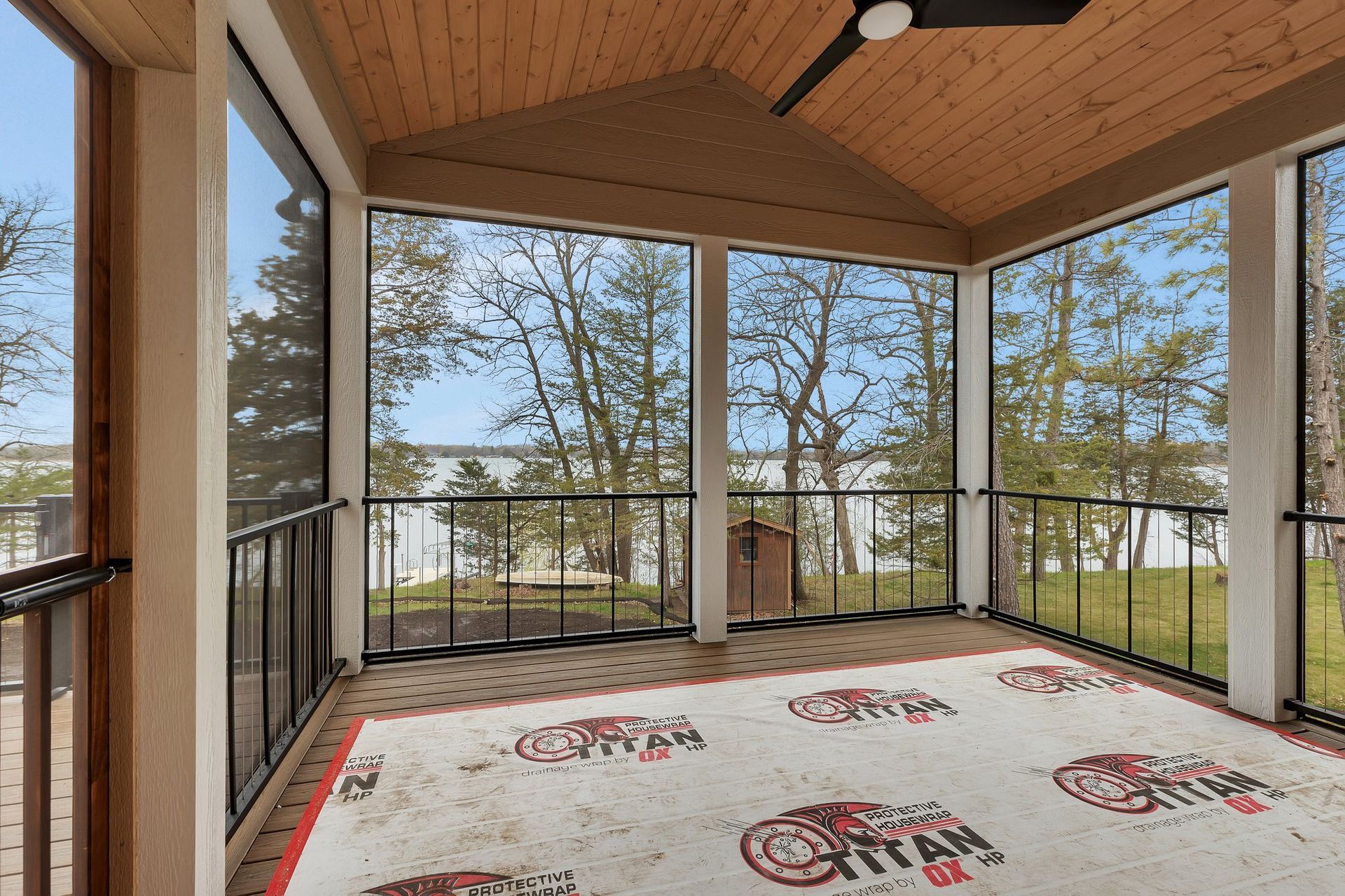 A screened in porch with a rug and a ceiling fan.