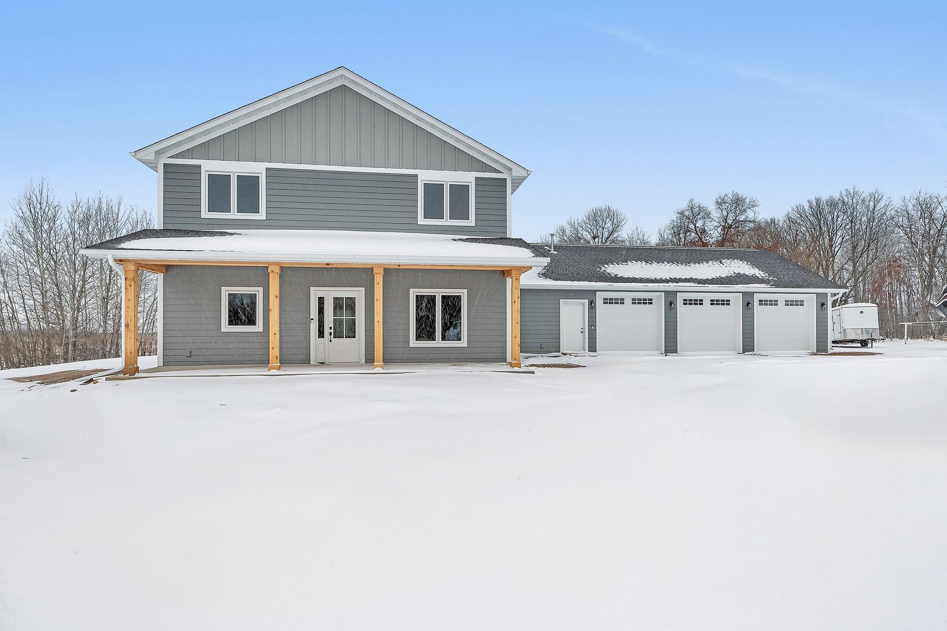 A large gray house is sitting in the middle of a snow covered field.
