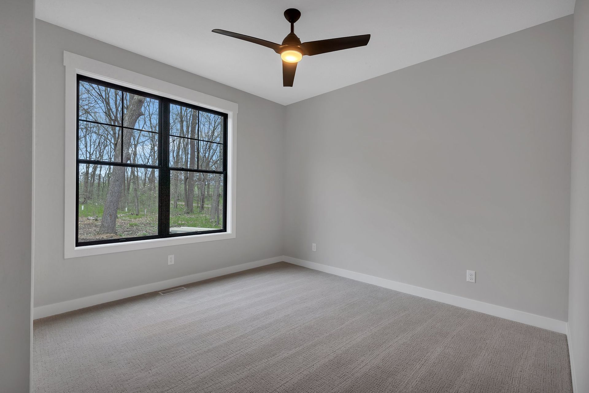 An empty bedroom with a ceiling fan and two windows.