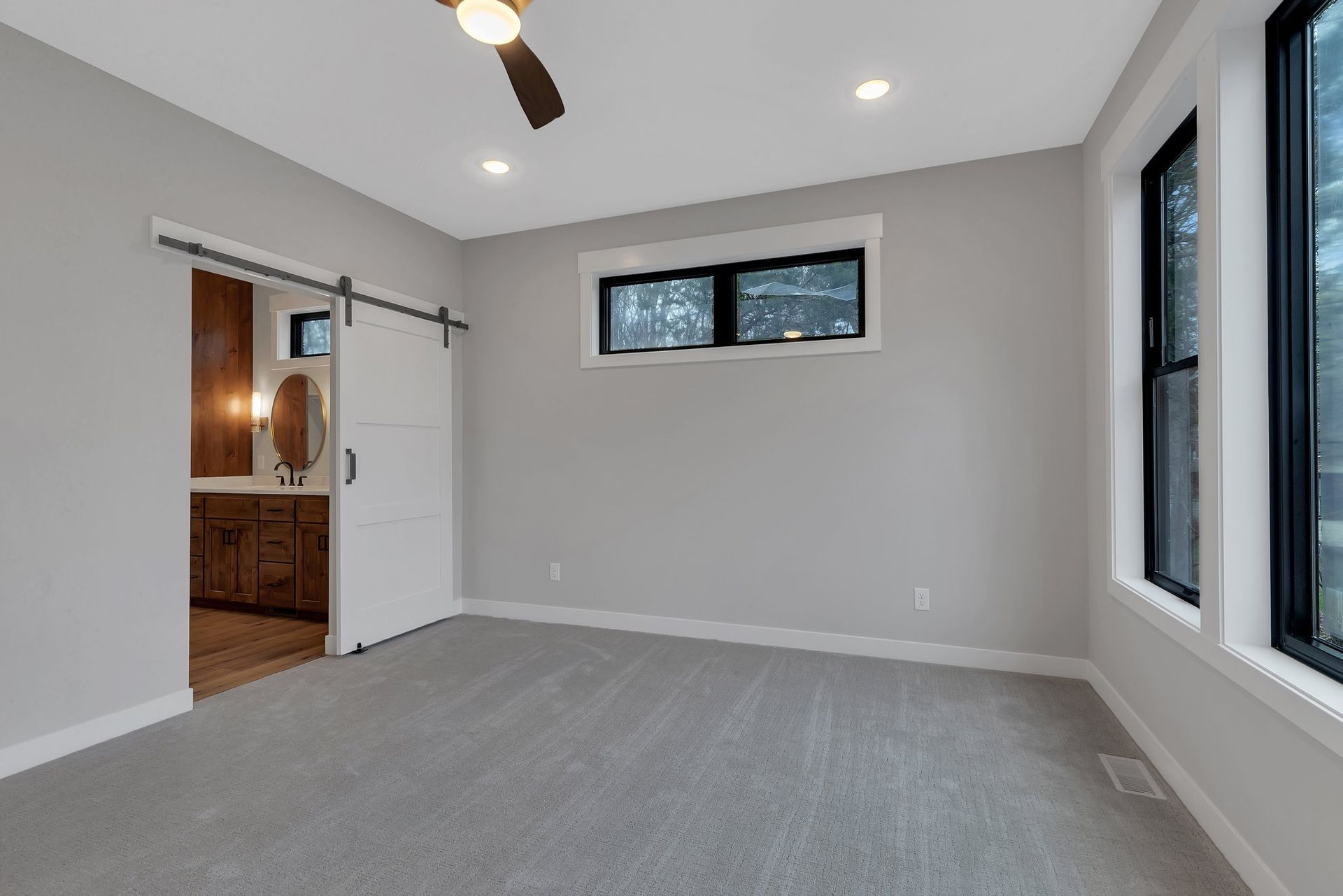 An empty bedroom with a sliding barn door and a ceiling fan.