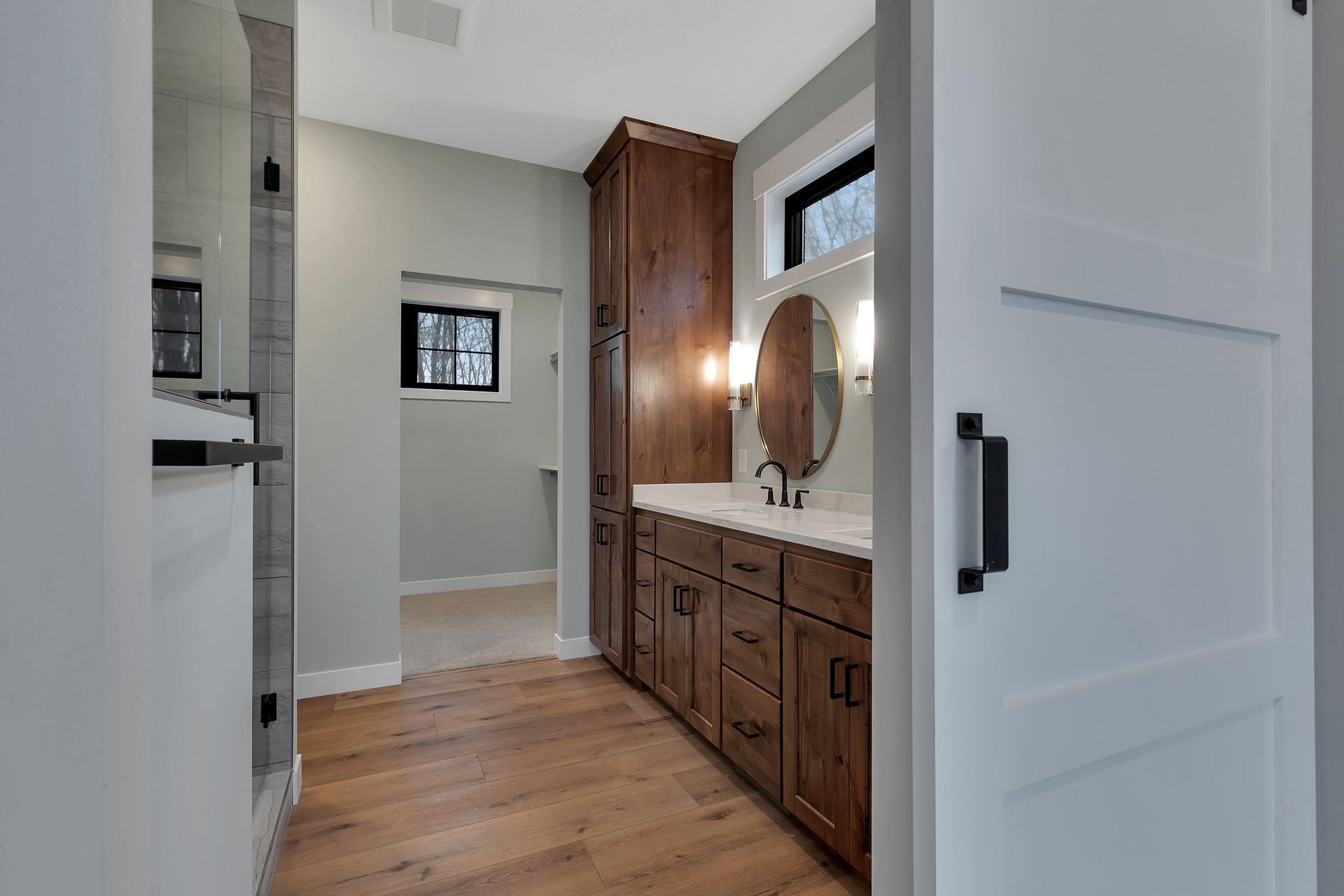 A bathroom with a sink , mirror , cabinets and hardwood floors.