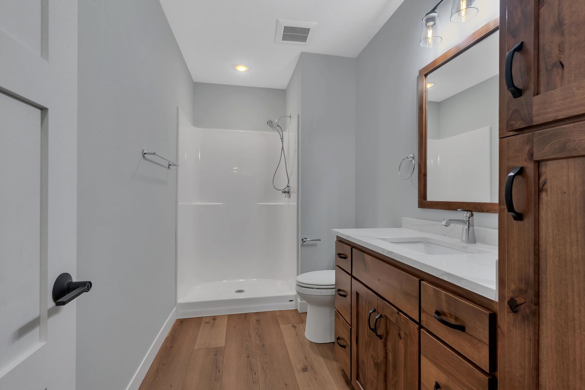 A bathroom with a toilet , sink , mirror and shower.